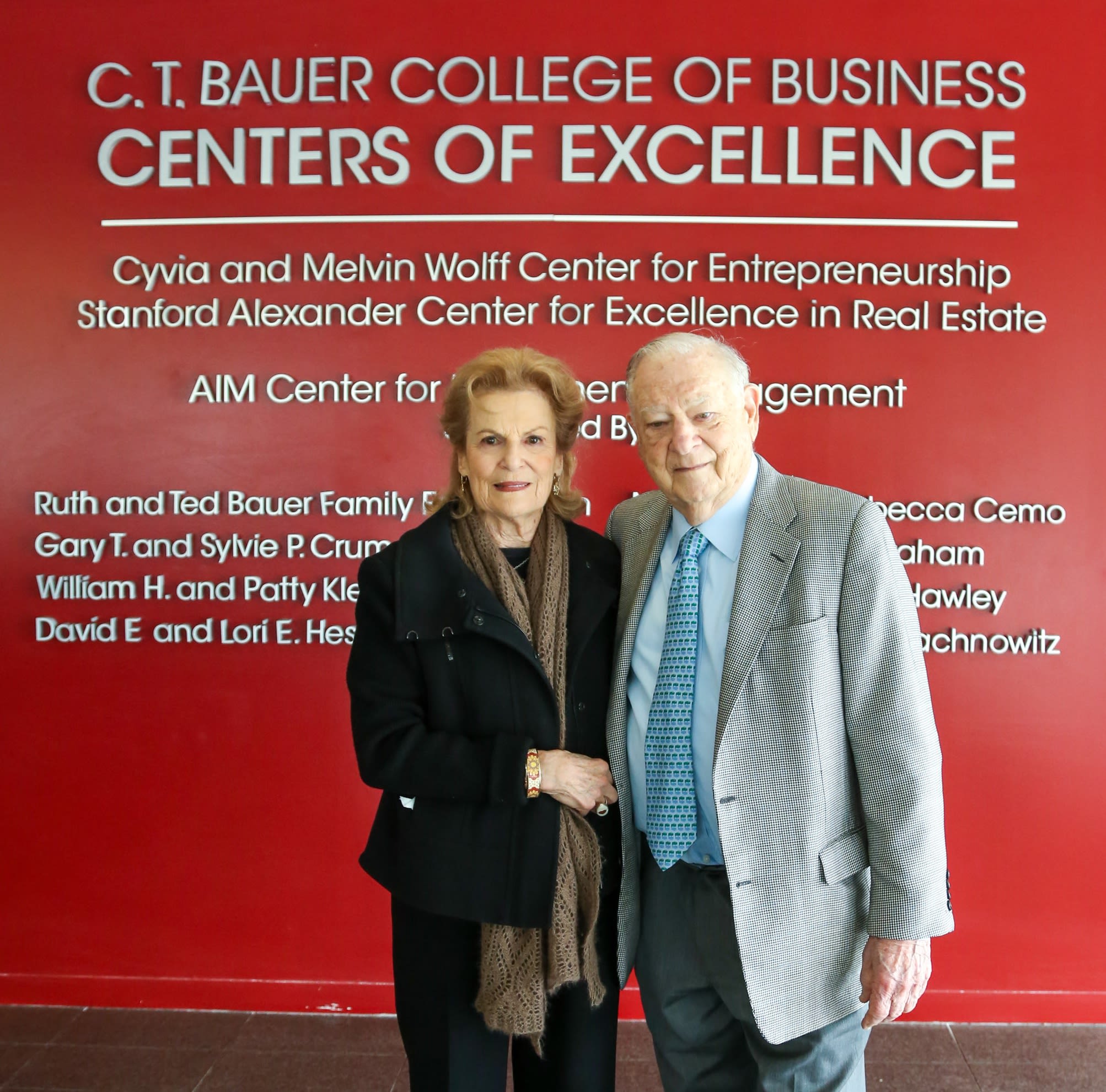 Joan and Stanford Alexander stand in front of signage for the C.T. Bauer College of Business Centers for Excellence.