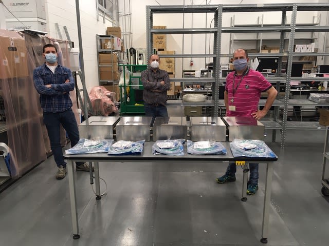 Three researchers wearing masks in front of five ventilators