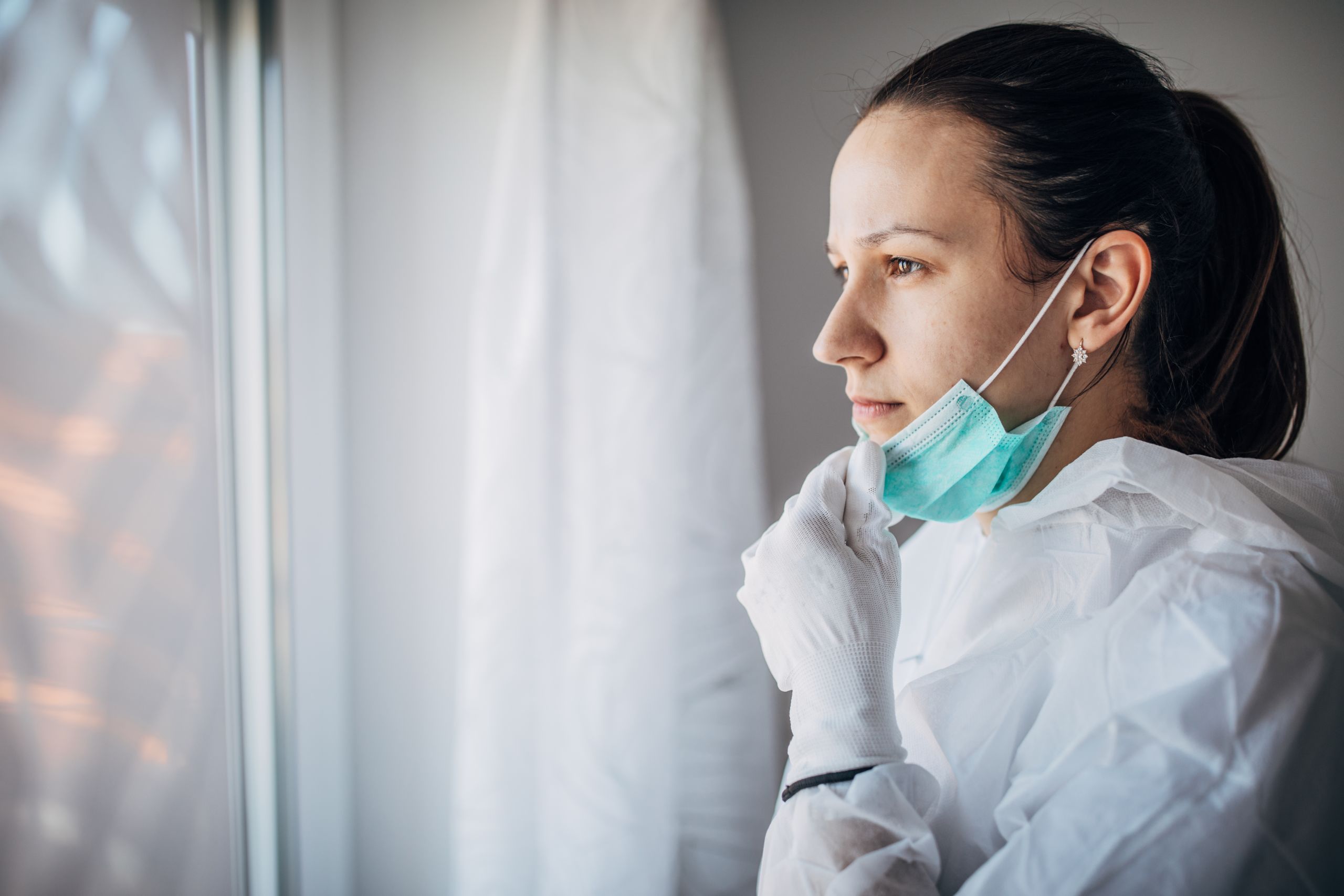 nurse looking out window with facemask drawn down.
