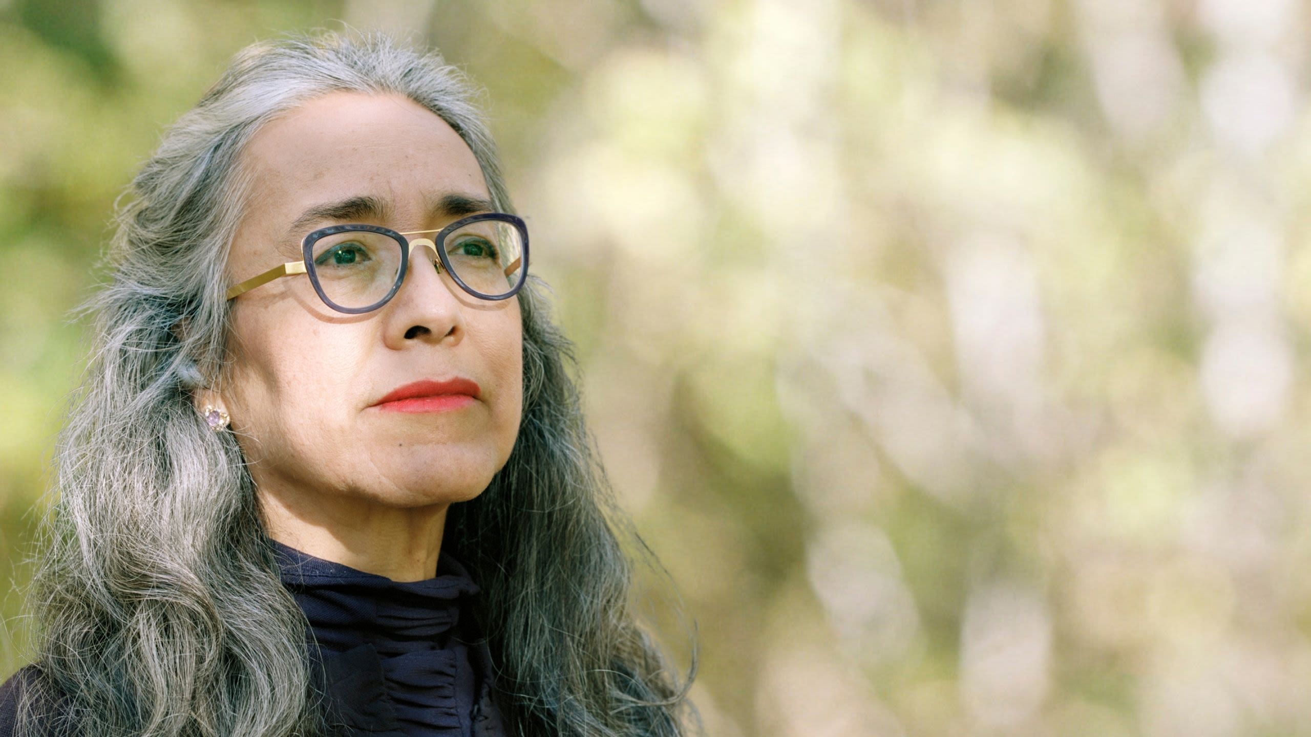 portrait of Cristina Rivera Garza in front of green trees looking off