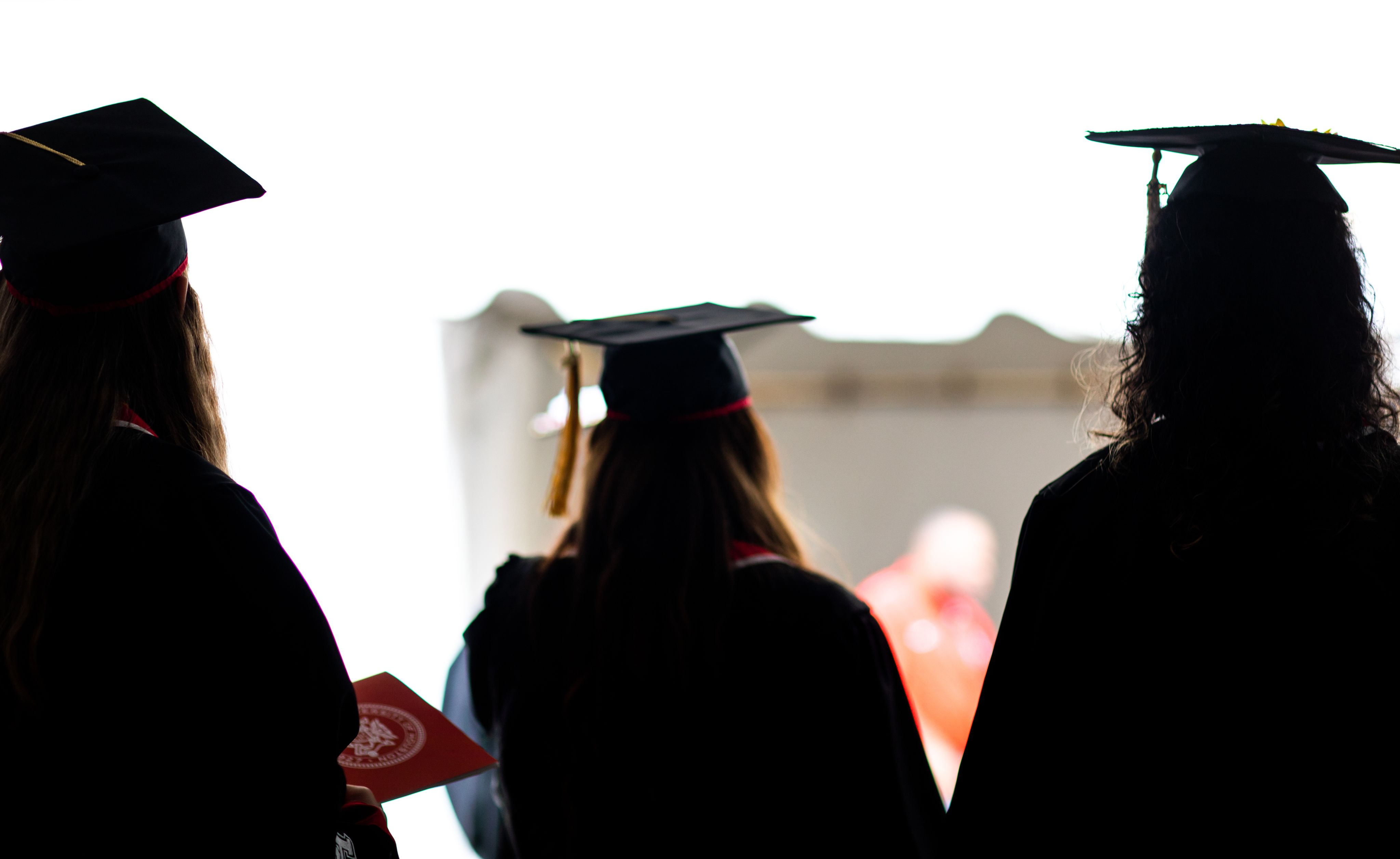 Three students wearing graduation caps and gowns walking out of a commencement ceremony.