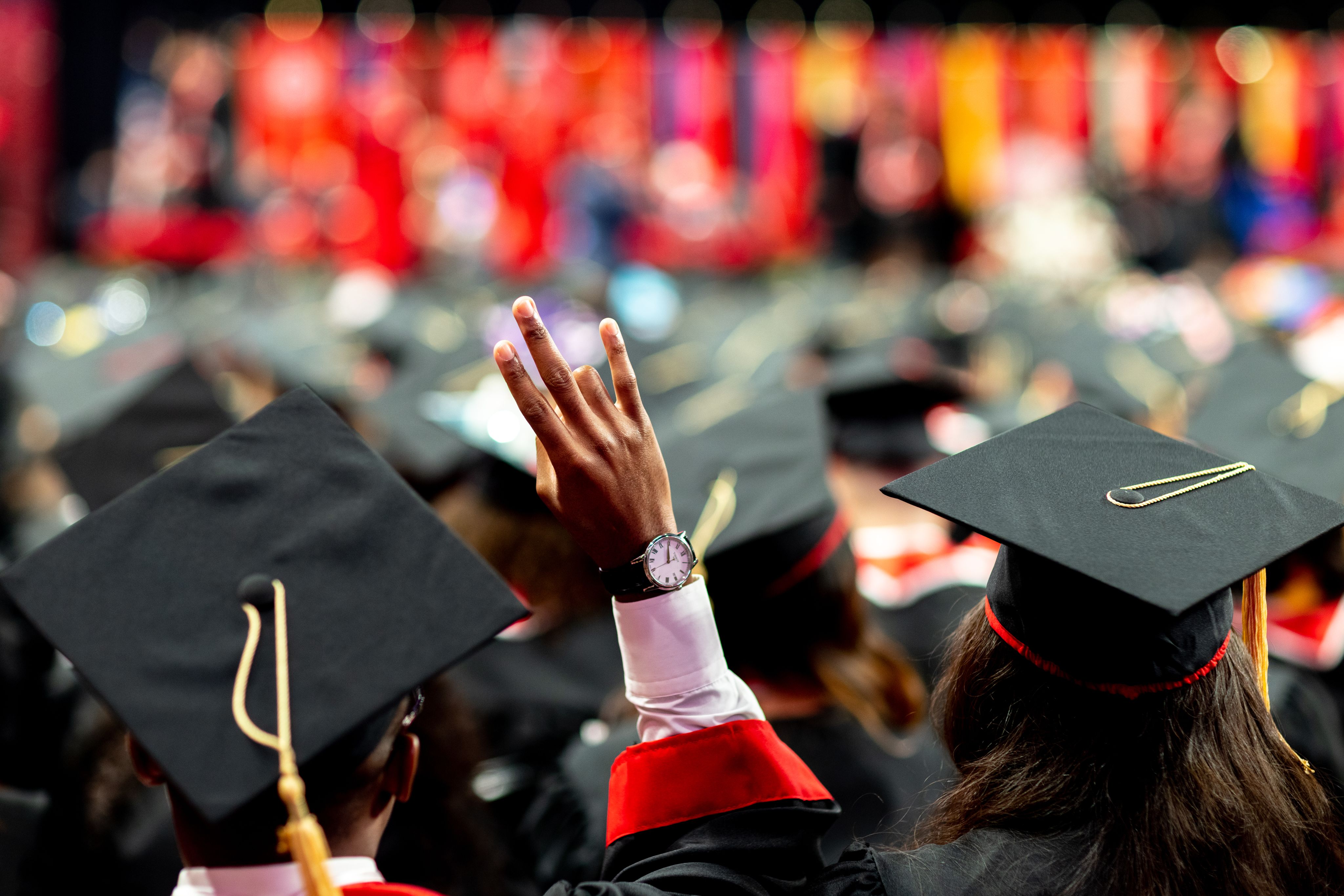 Graduating student is seen from the back with his hand raised, making a coog sign.