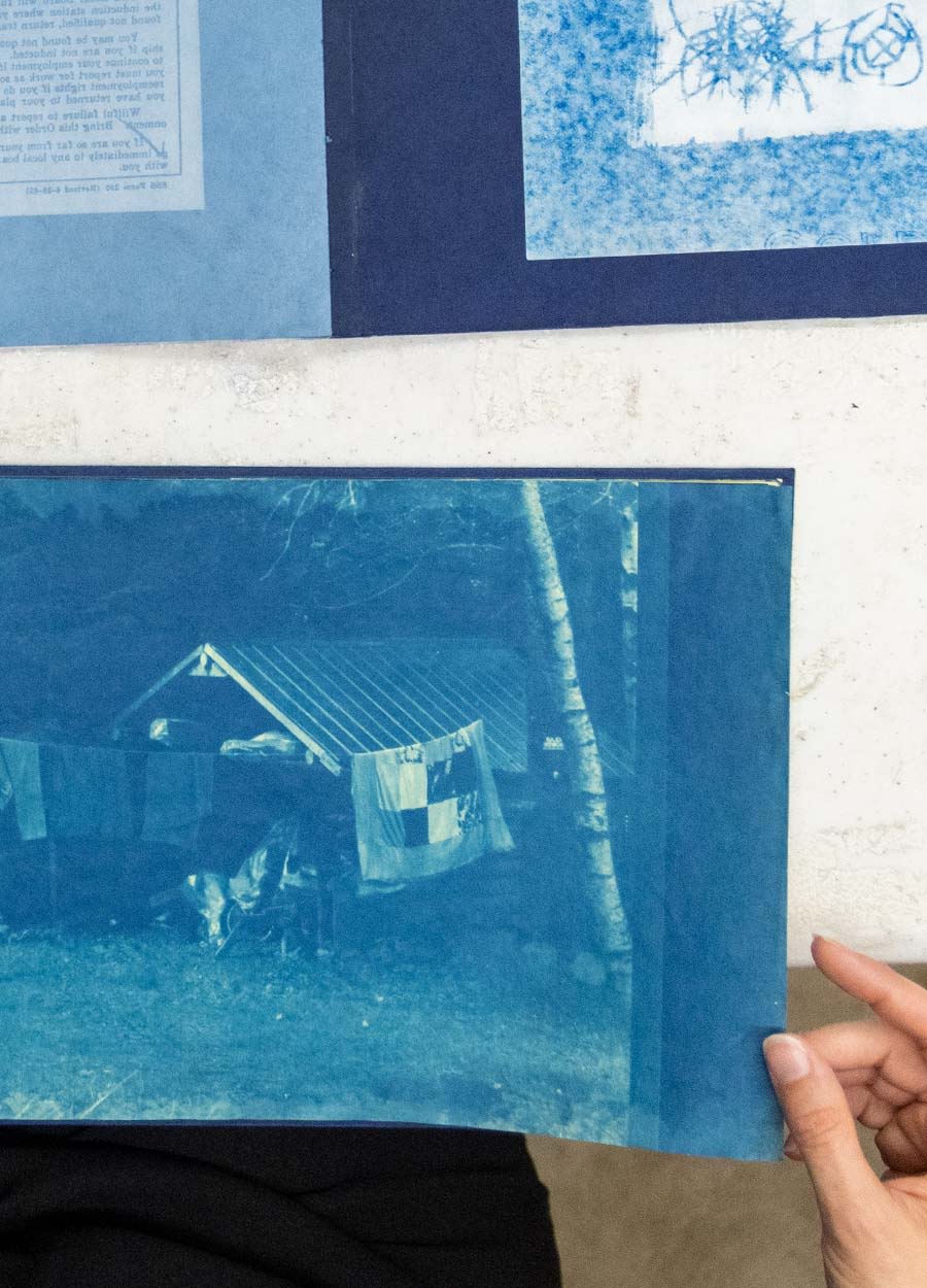 Anderson-Staley, flipping through a book with blue images, pauses on an image of a shed and items hanging on a clothes line. She uses cyanotype, an alternative photographic process, in many of her pieces.
