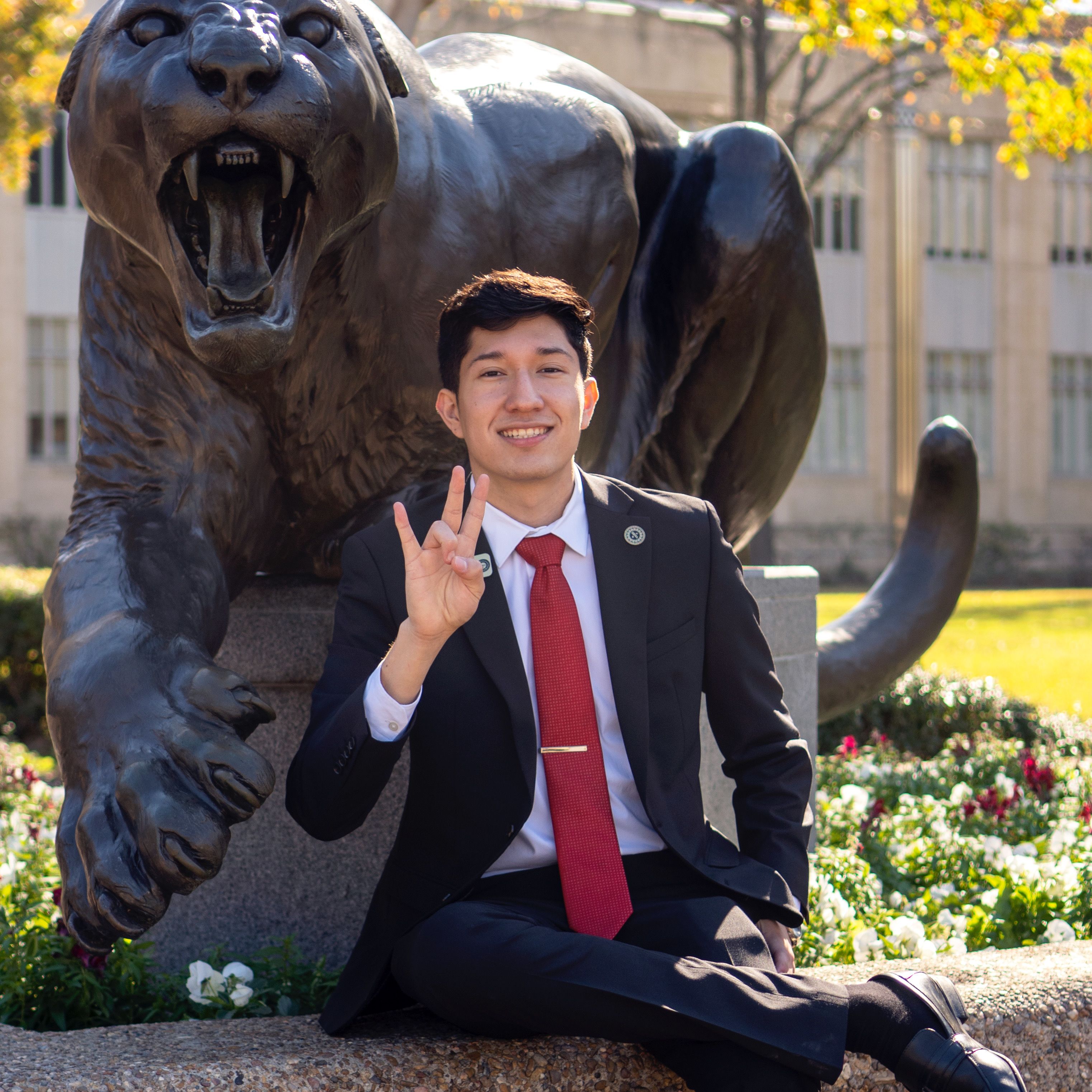 Student with dark suit sitting front of statue.