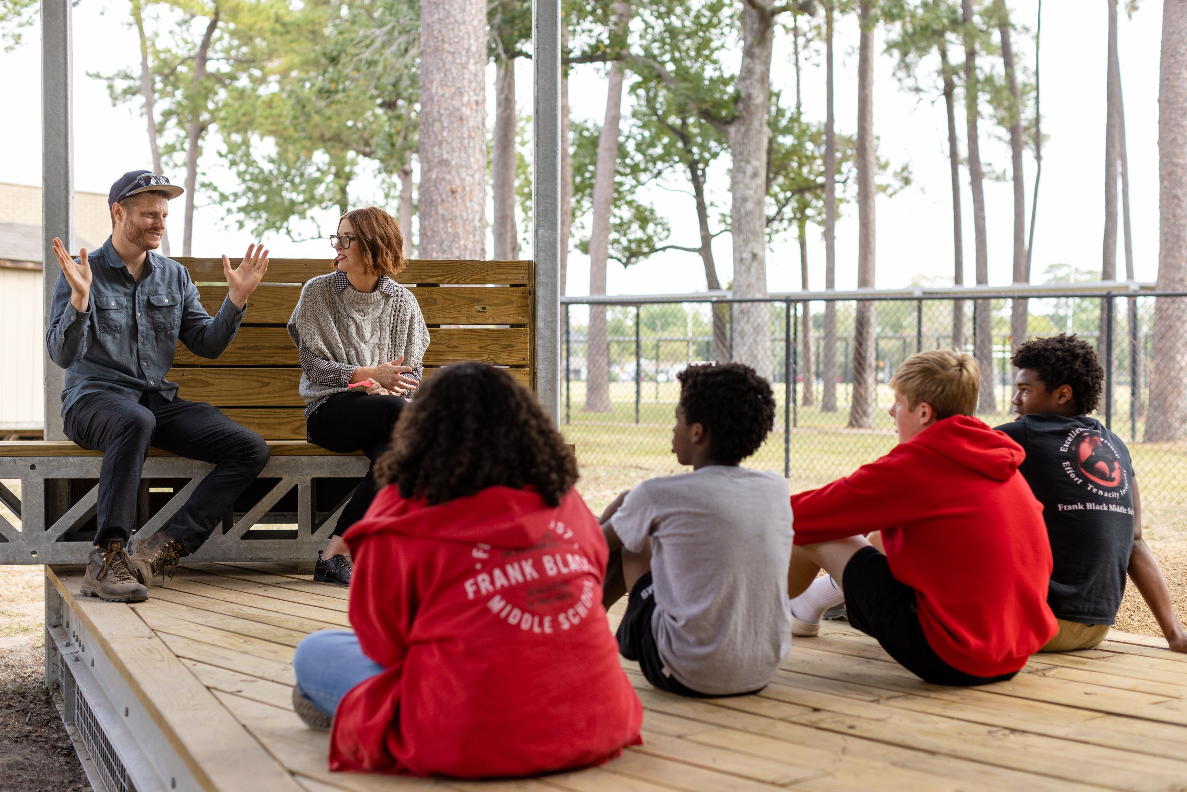 Two adults speaking to four middle school students in an outdoor classroom.