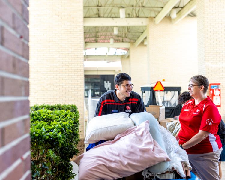 Staff and students carrying bin of pillows and bedding into residence hall at move in.