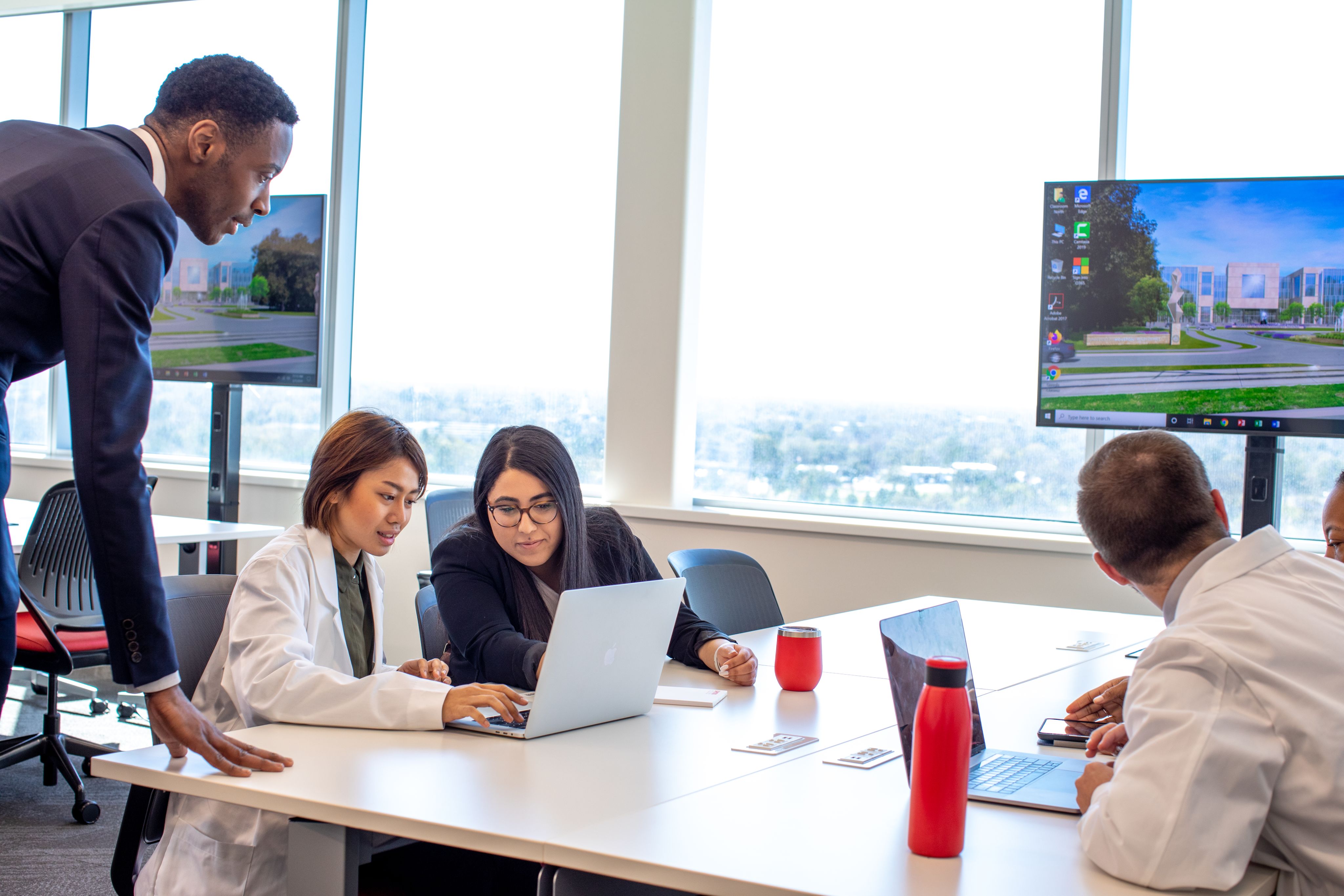 Students look at a computer with a professor peering over their shoulder