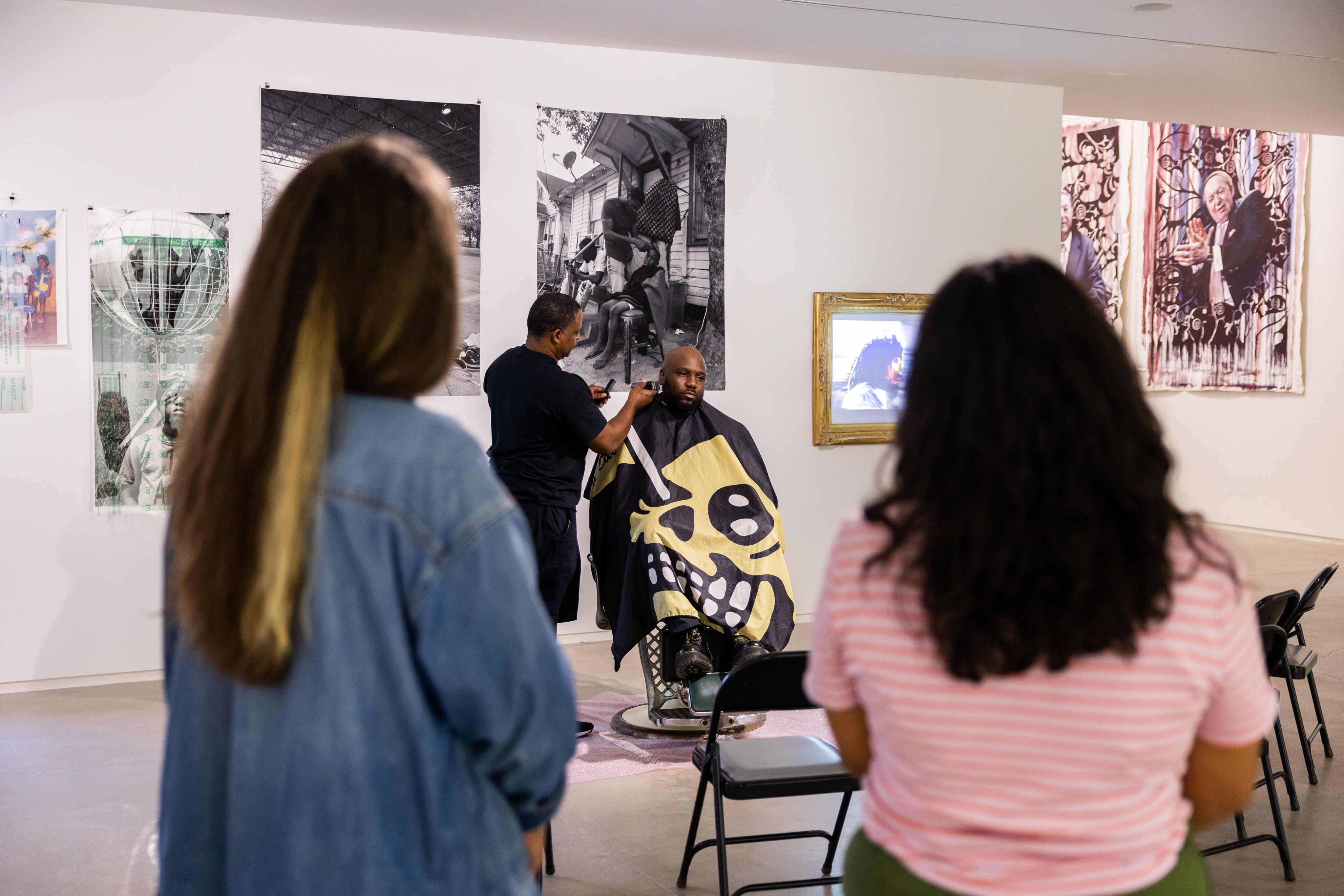 Museum patrons watch Brian Ellison get a haircut in a barber chair at his senior thesis at blaffer art museum
