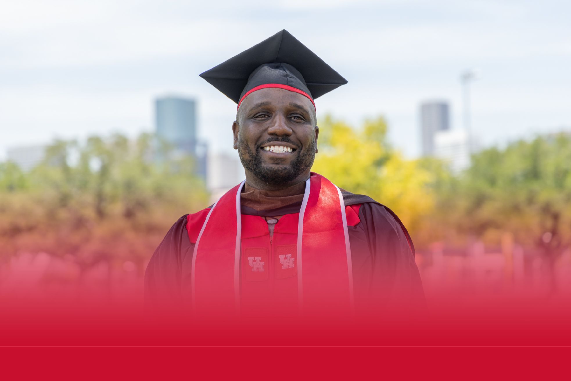 Brian Ellison poses in his graduation gear and smiles with houston in the background
