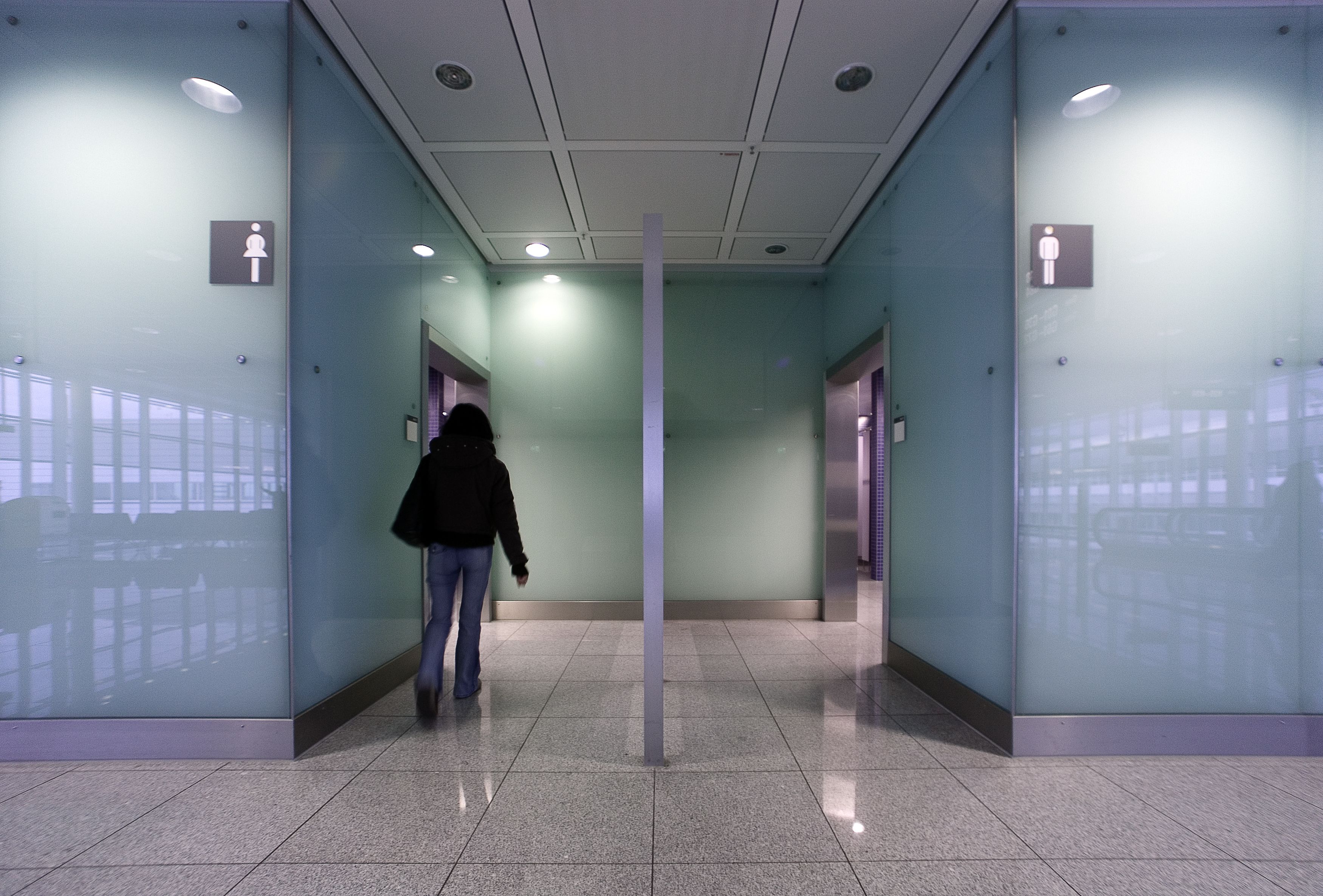 young woman walking into public restroom, back to camera.