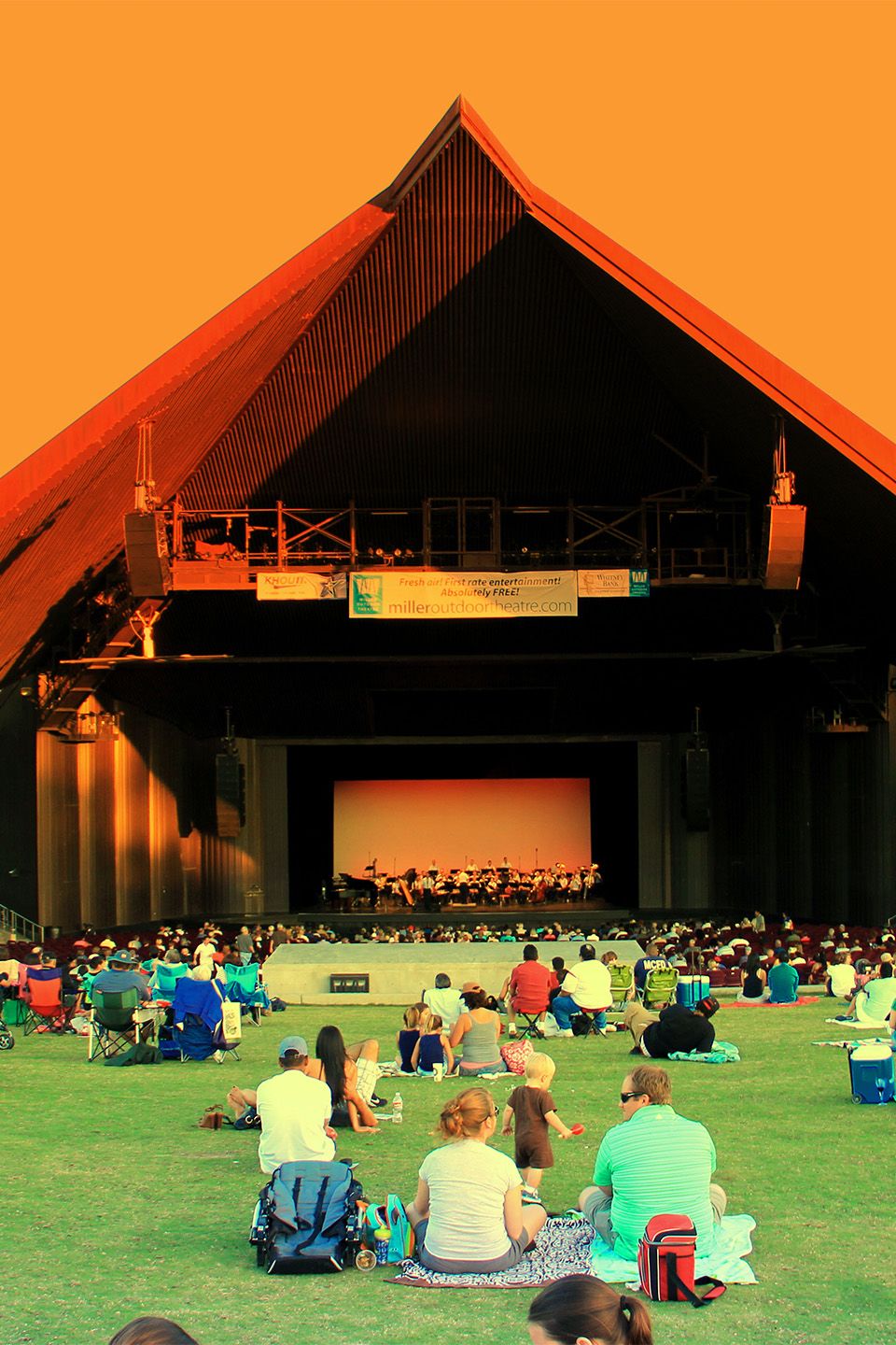 A wide shot of families on the law watching a performance at miller outdoor theater