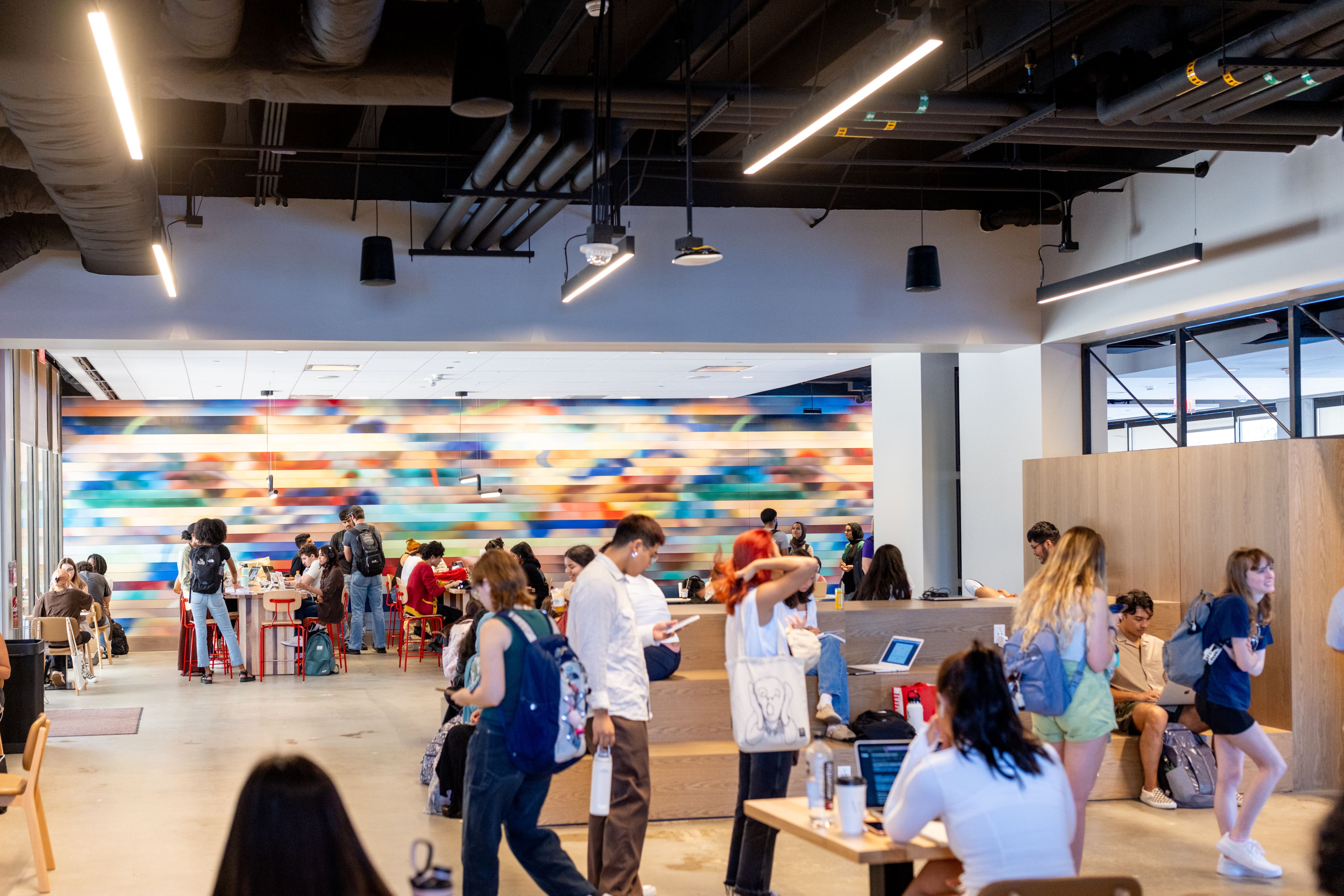 Interior view of Cougar Grounds coffeehouse at the UH Hilton College. Many students enjoy the atmosphere. A colorful mural is on a wall in the background.