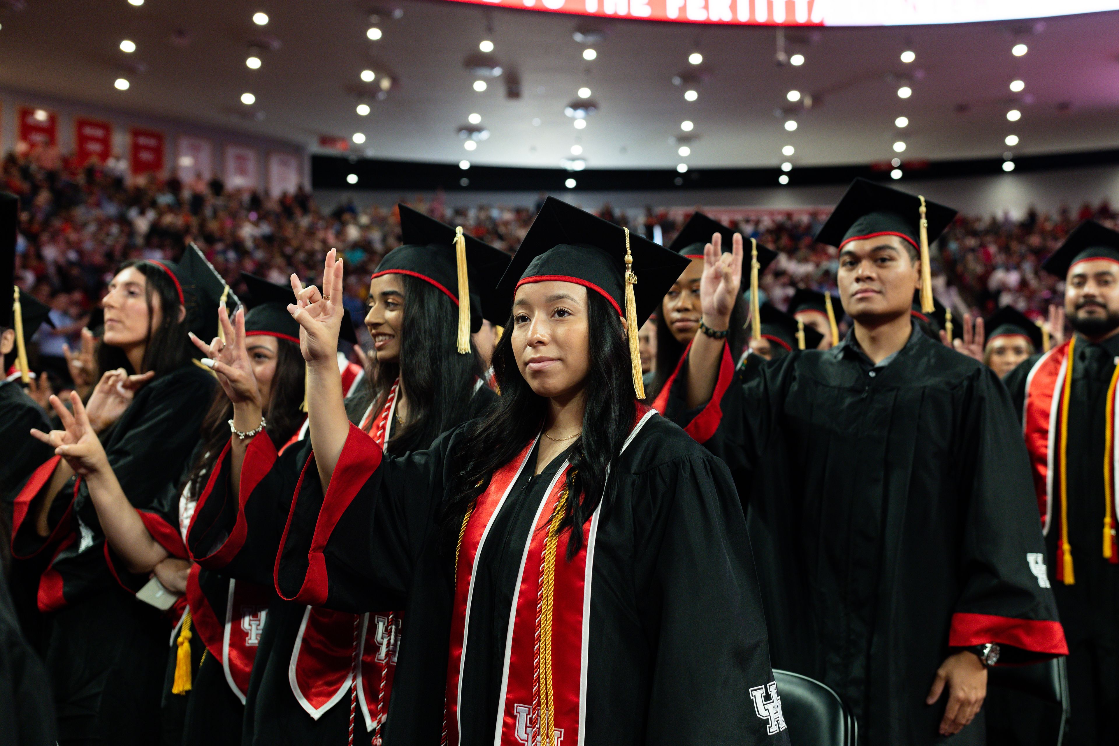 Several UH graduates dressed in caps and gowns with red UH stoles make the Cougar Sign with their hands