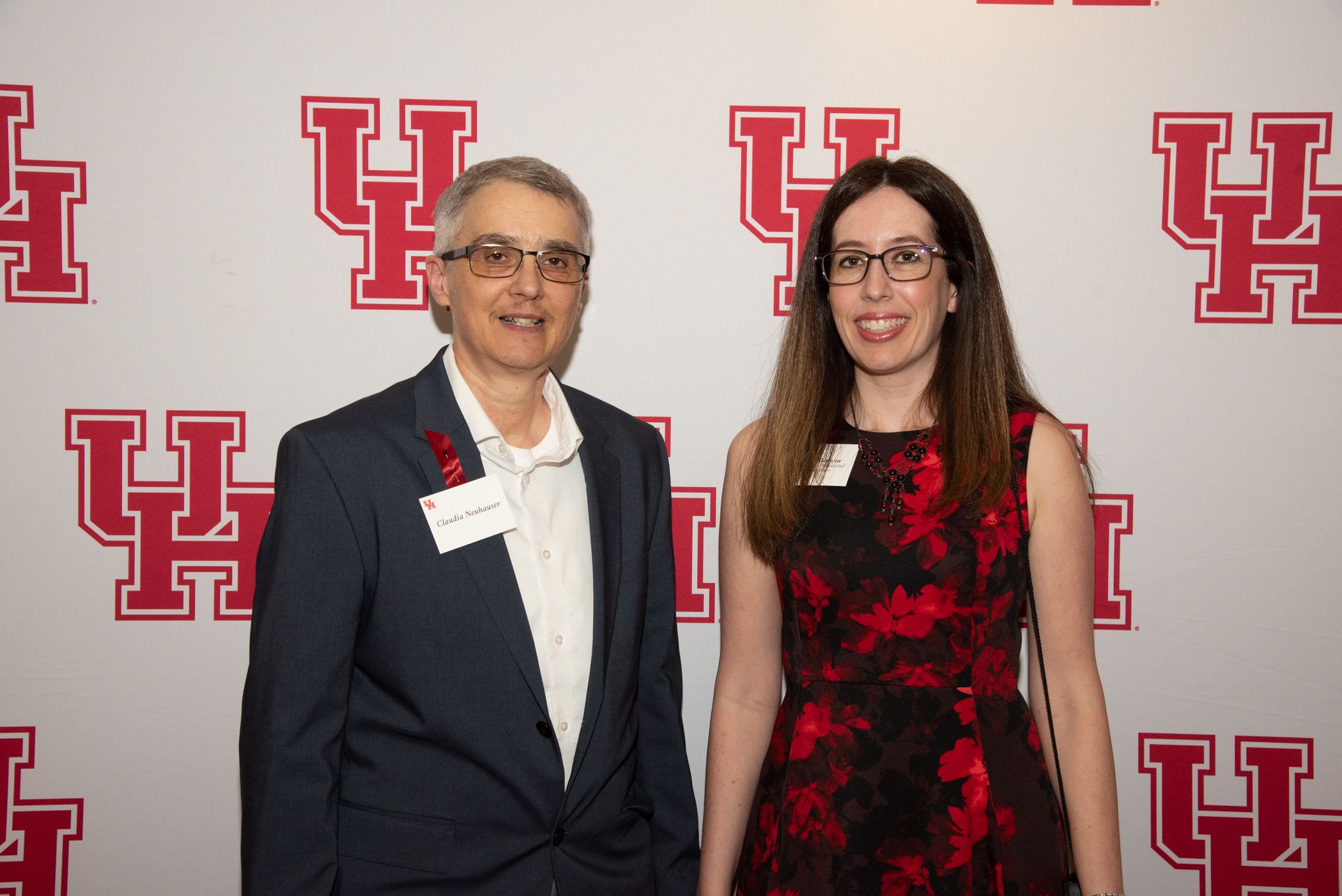 Standing in front of a white background with red UH logos are Claudia Neuhauser, vice president for research, wearing a dark suit coat and white shirt and Administrative Professional Award winner Ashley Merwin who is wearing a red and black dress..