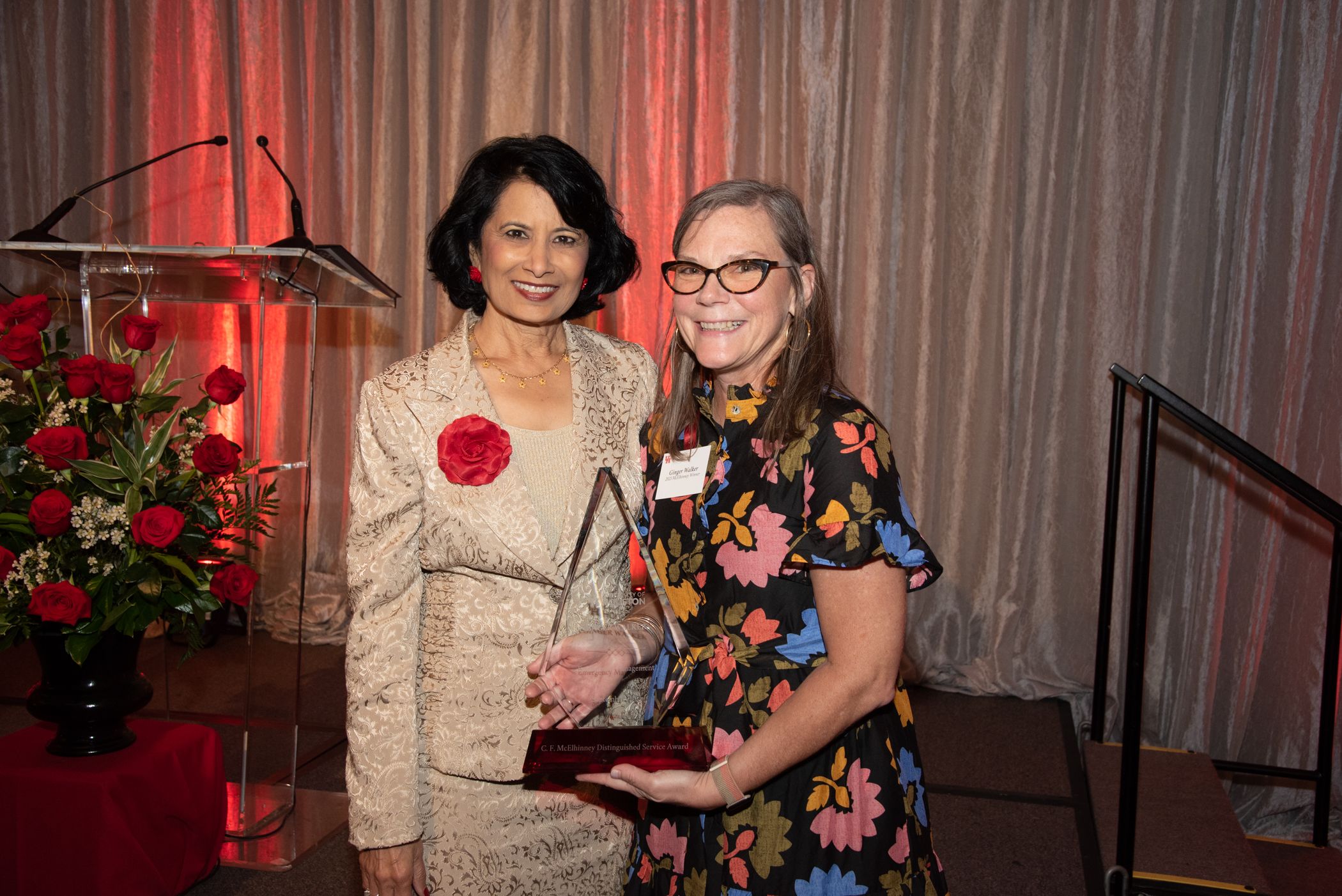 Ginger Walker, director of Emergency Management, holding her crystal award and standing to the right of President Renu Khator who is wearing a gold suit.