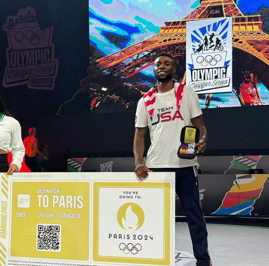 Photo of Jeffrey Louis shortly after qualifying for the 2024 Olympics. He is posing in front of a sign and wearing a Team USA t-shirt.