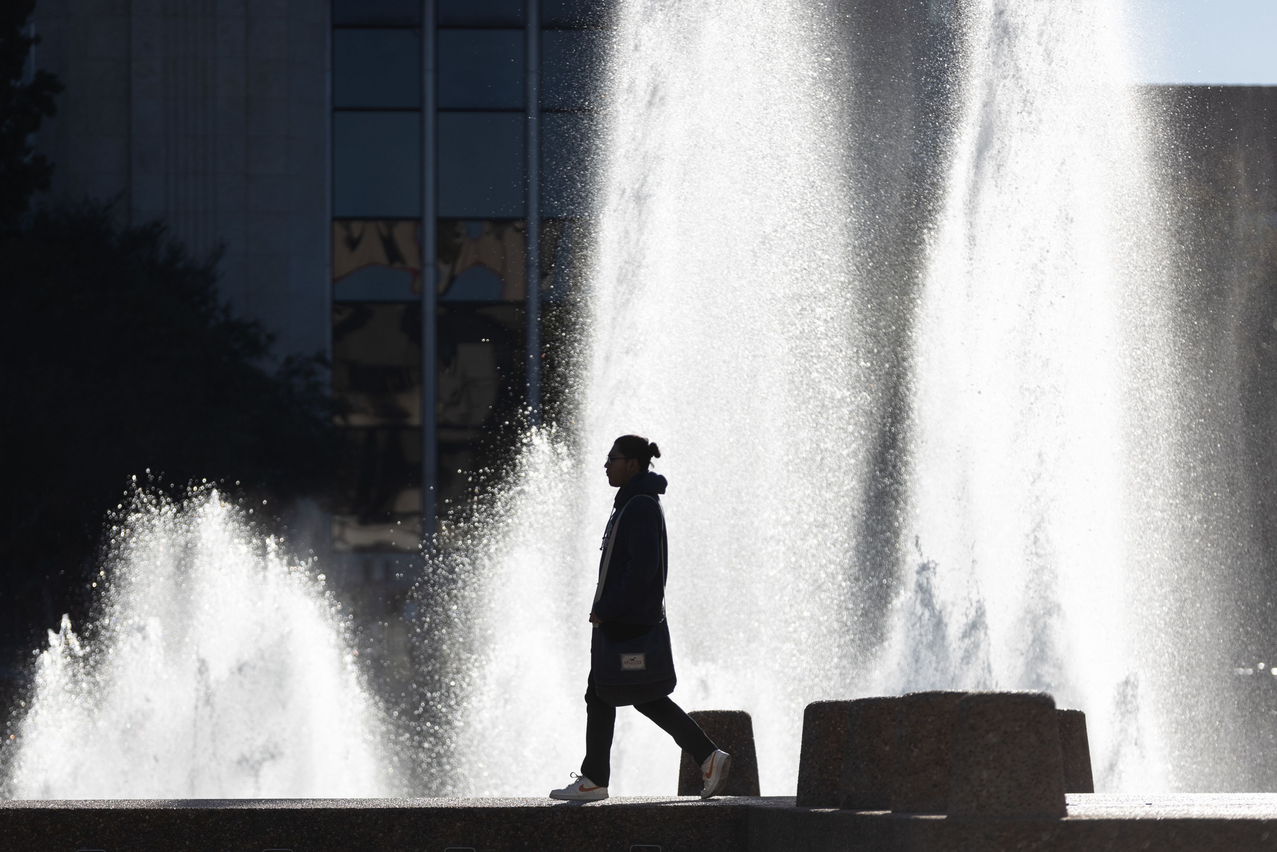 silhouette of person walking in front of Cullen fountain with the water behind them