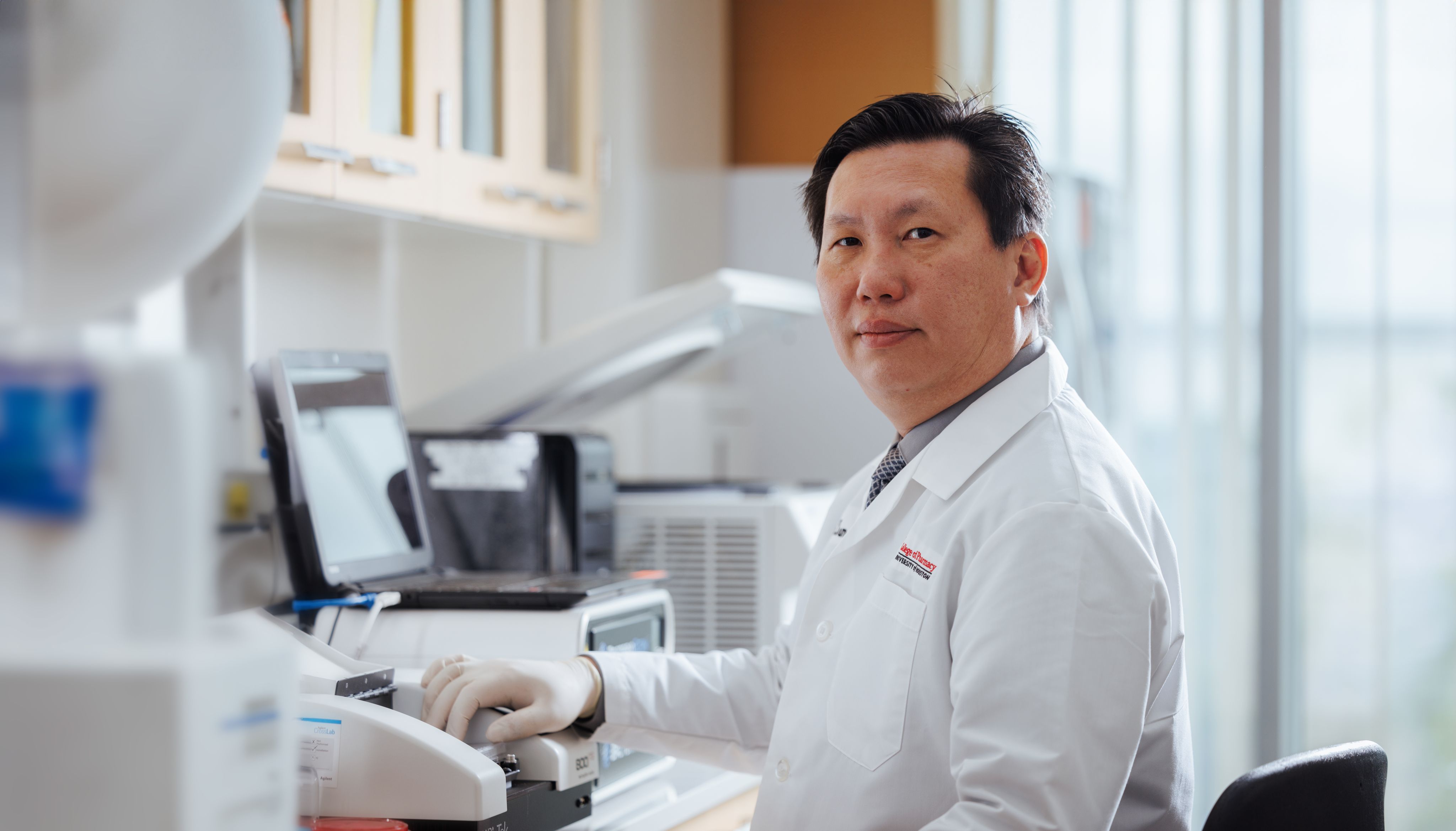 Vincent Tam wearing a lab coat stands confidently, embodying professionalism and expertise in a scientific environment.
