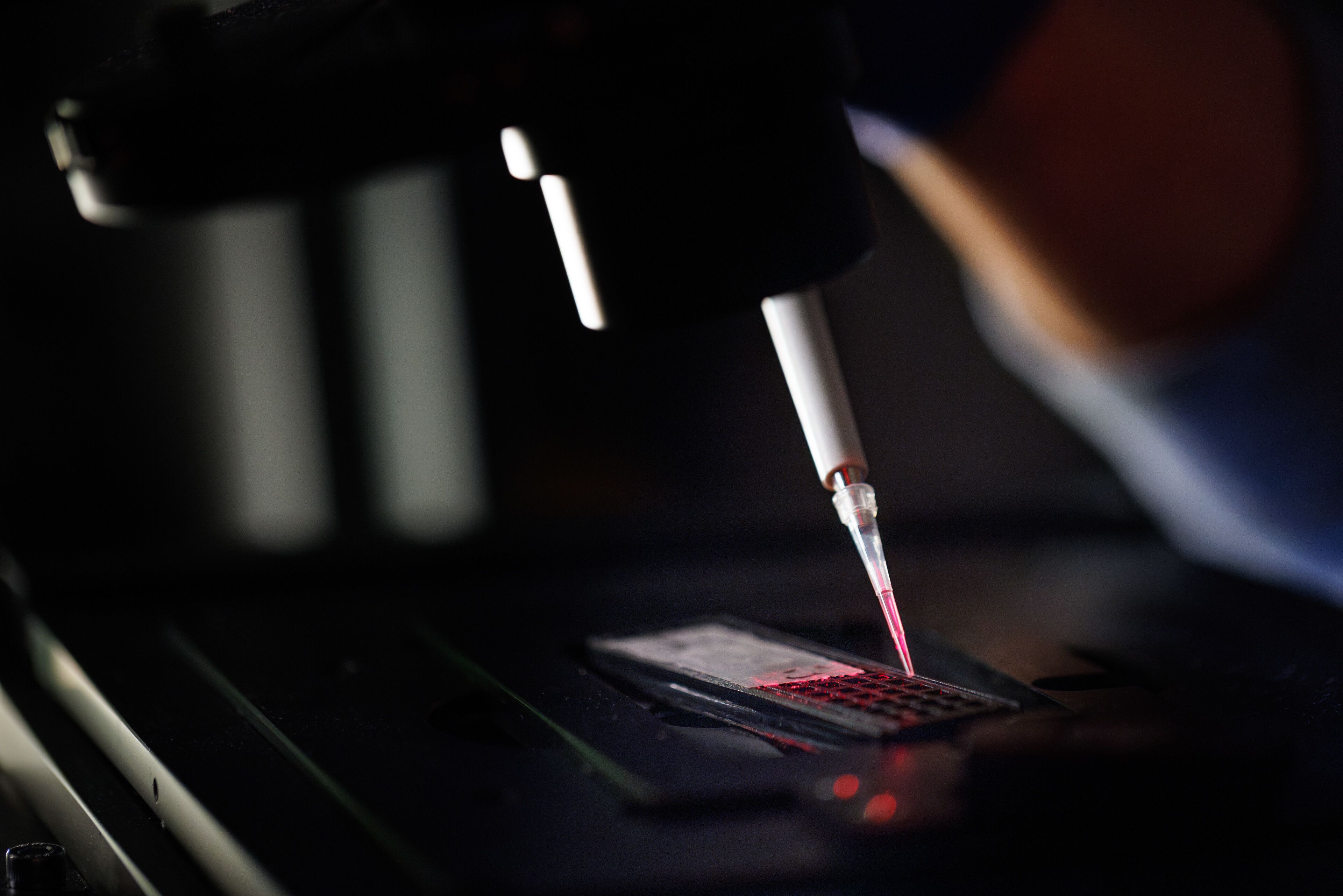 A person examines a red object through a microscope, focusing intently on the details of the specimen.