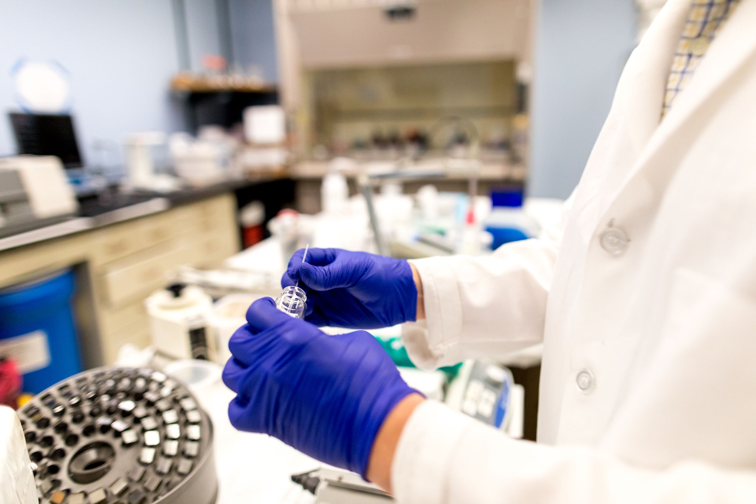 hands with purple gloves handling glass vile in lab