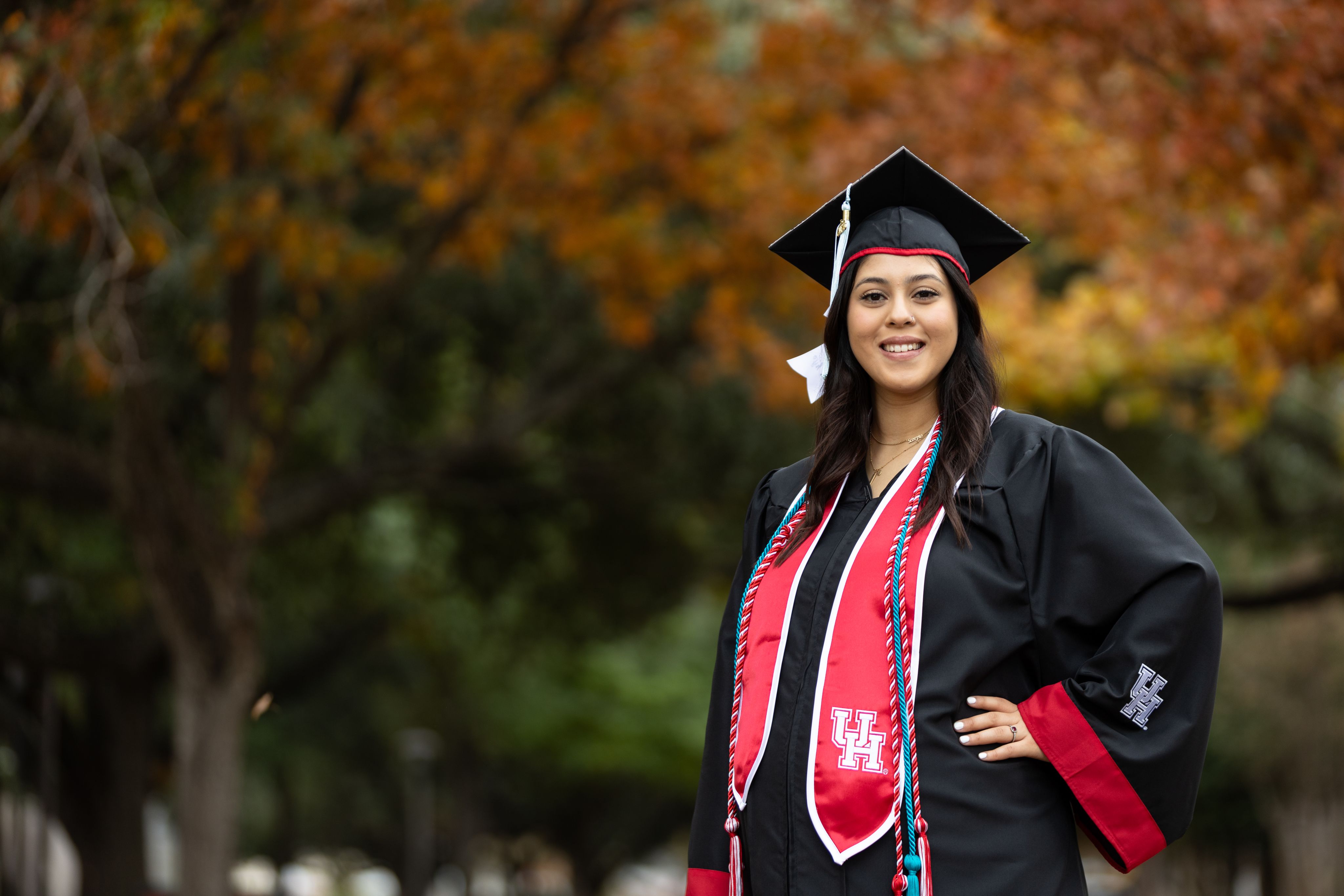Women wearing black graduation cap and gown standing in front of trees