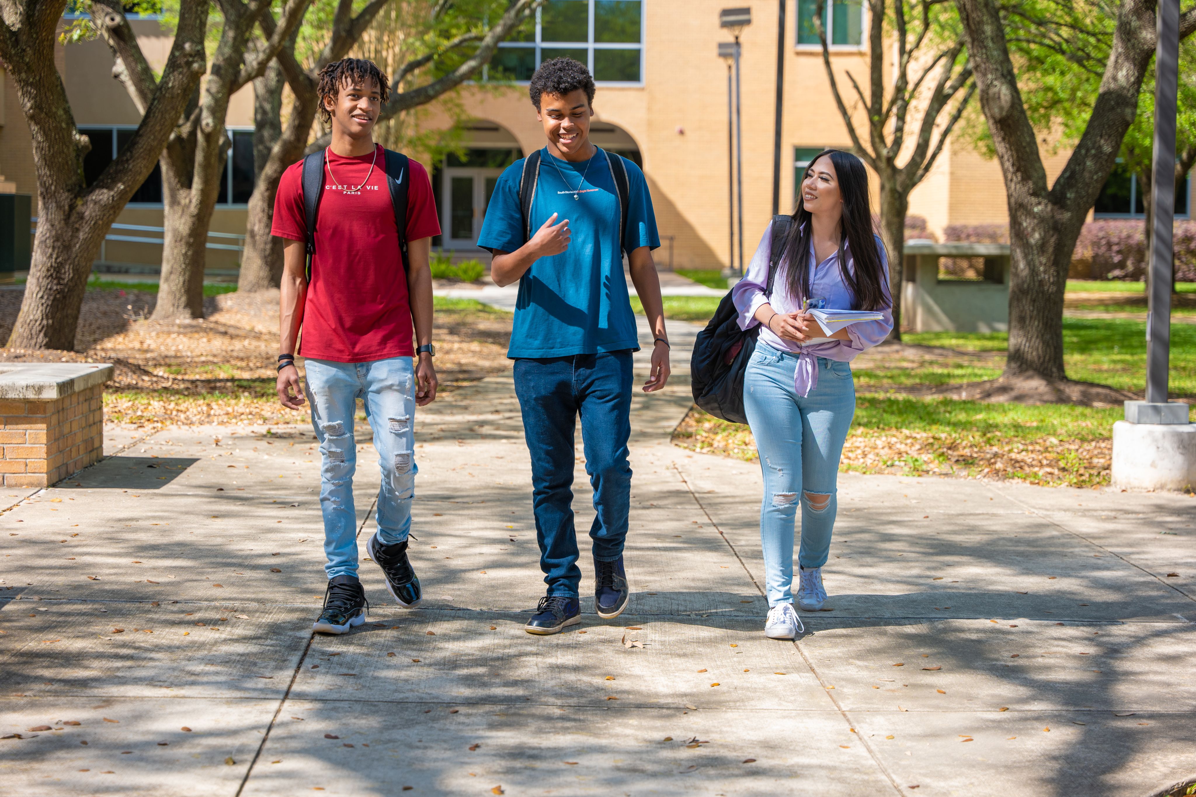 Two males in T-shirts walking with female in blouse and jeans