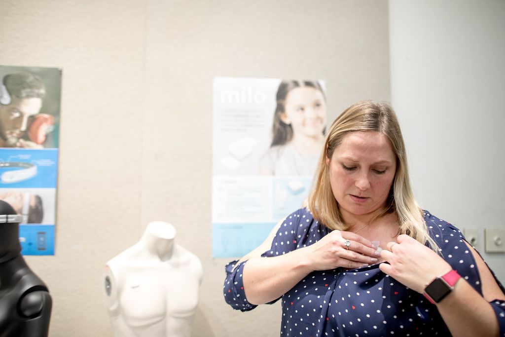 Woman puts tab on shoulder to demo device.