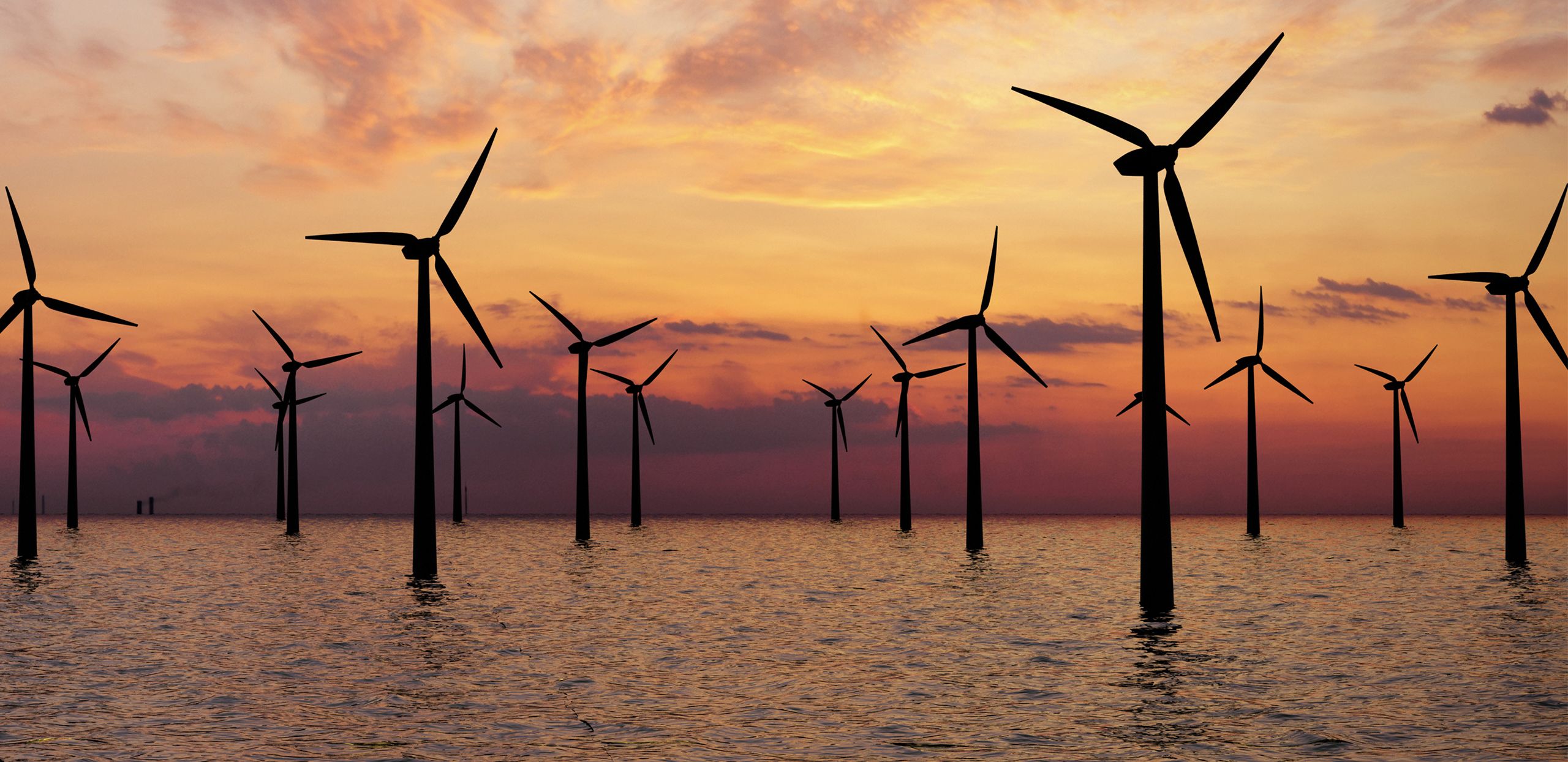 An oil rig in the middle of a body of water, surrounded by wind turbines.