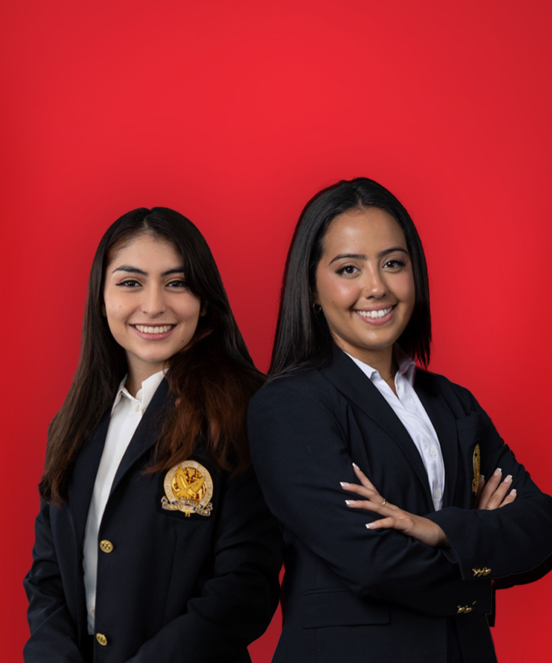 Portrait of students Arianna Chavarria and Fernanda Ruelas wearing honors jackets against a red background.