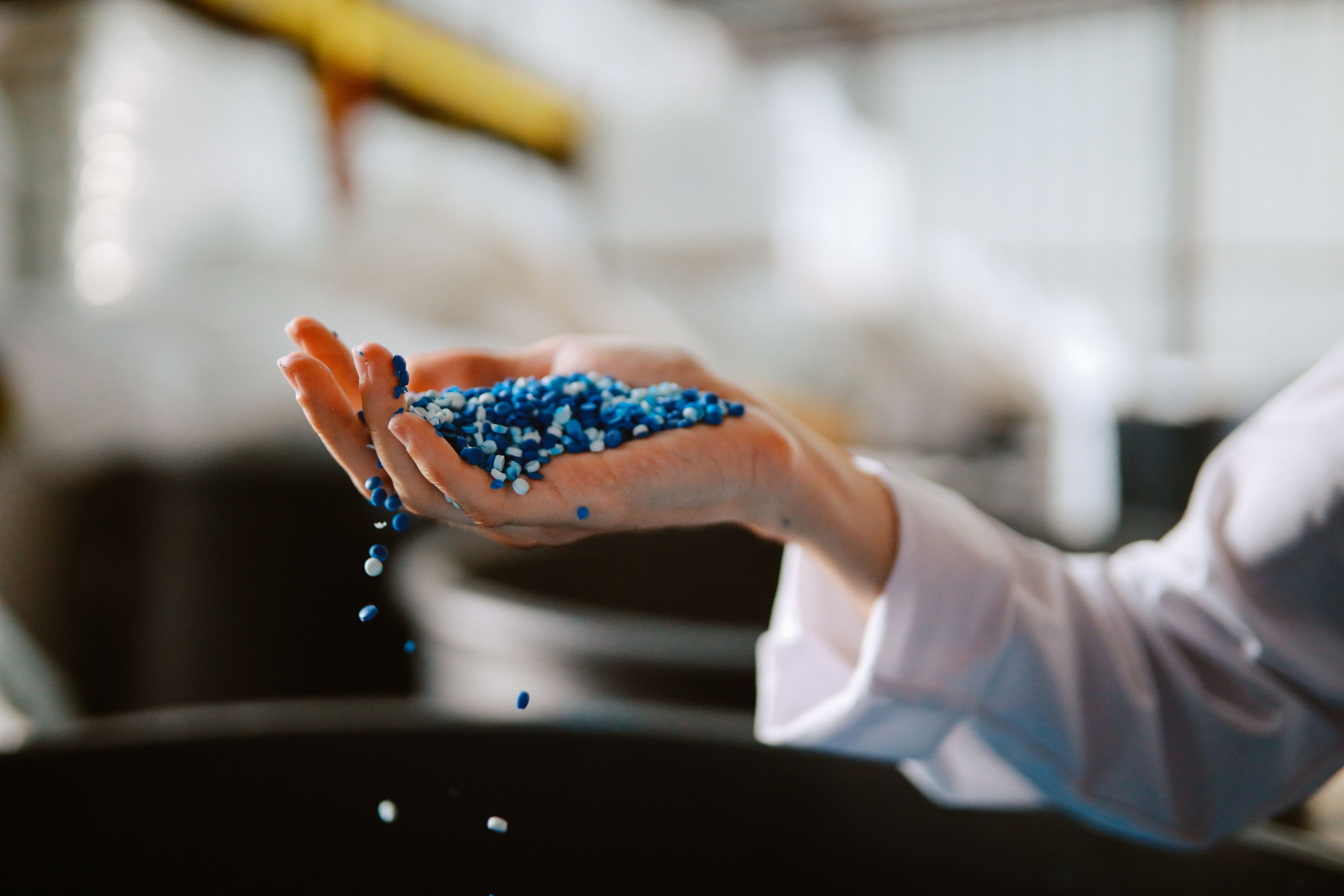 Photo of an outstretched arm wearing a lab coat and holding a handful of plastic pellets.