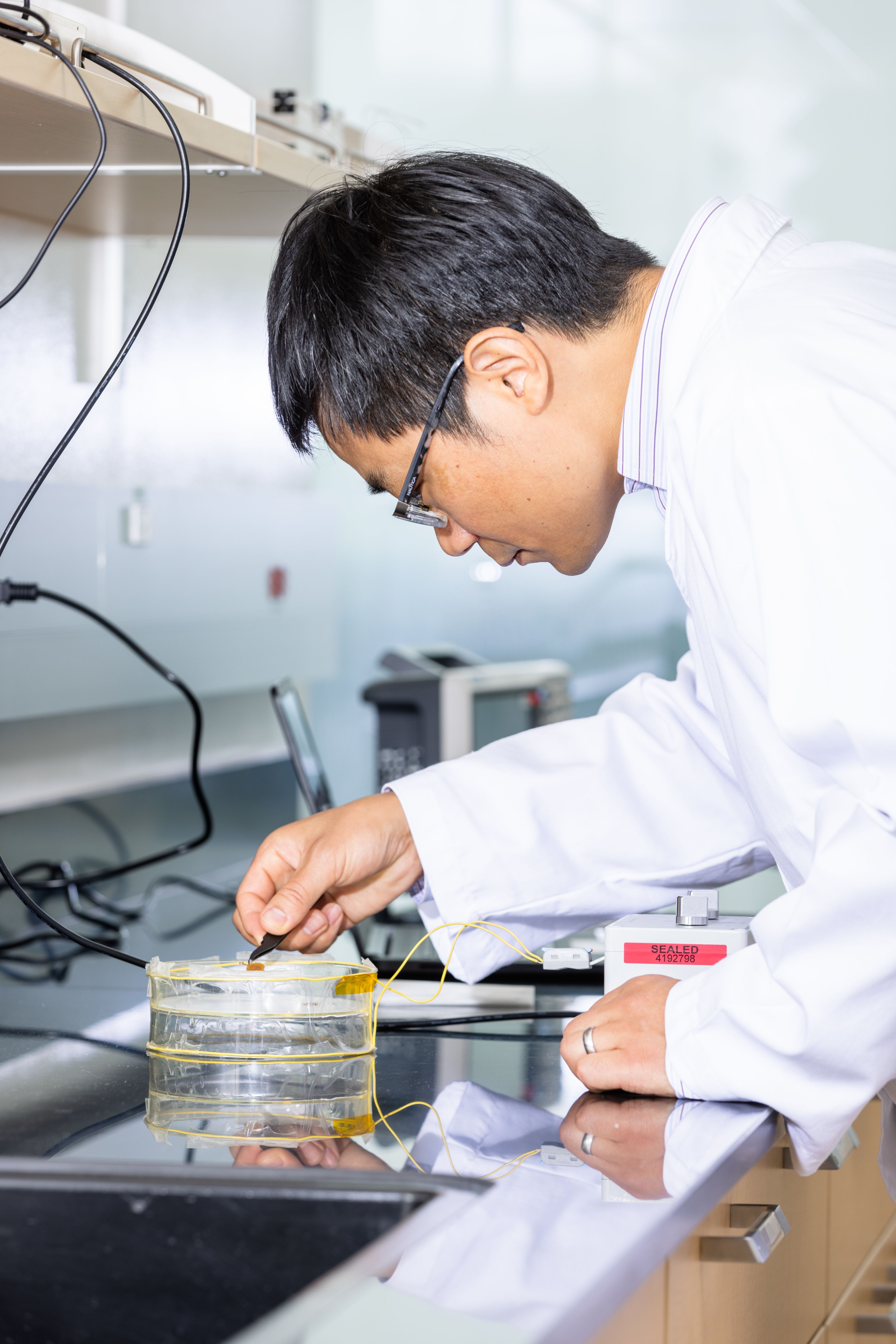 Zhengwei Li in a lab coat & glasses working on bio sensors