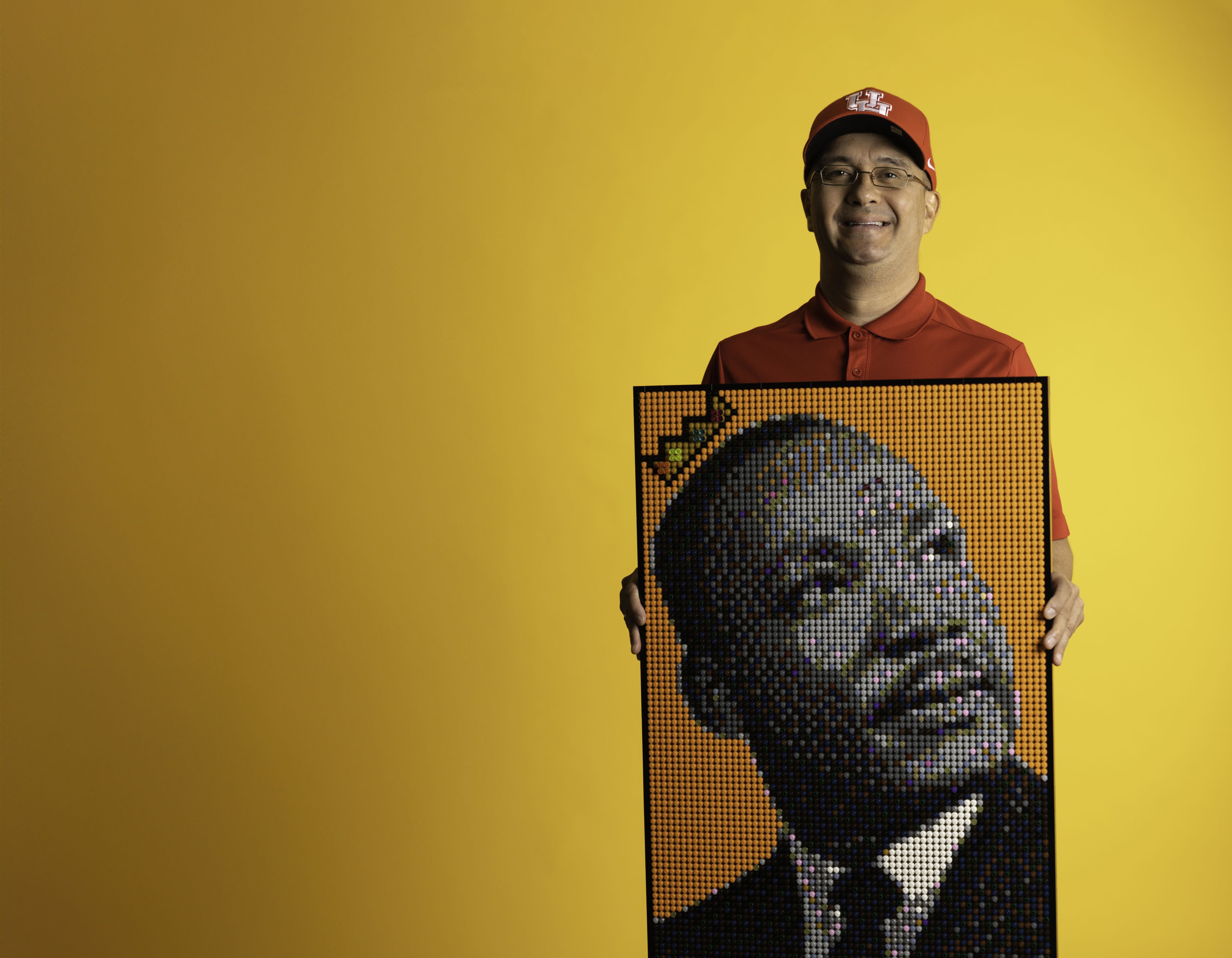Gregory Jonason standing in front of a yellow background, holding his lego portrait on Martin Luther King Jr.