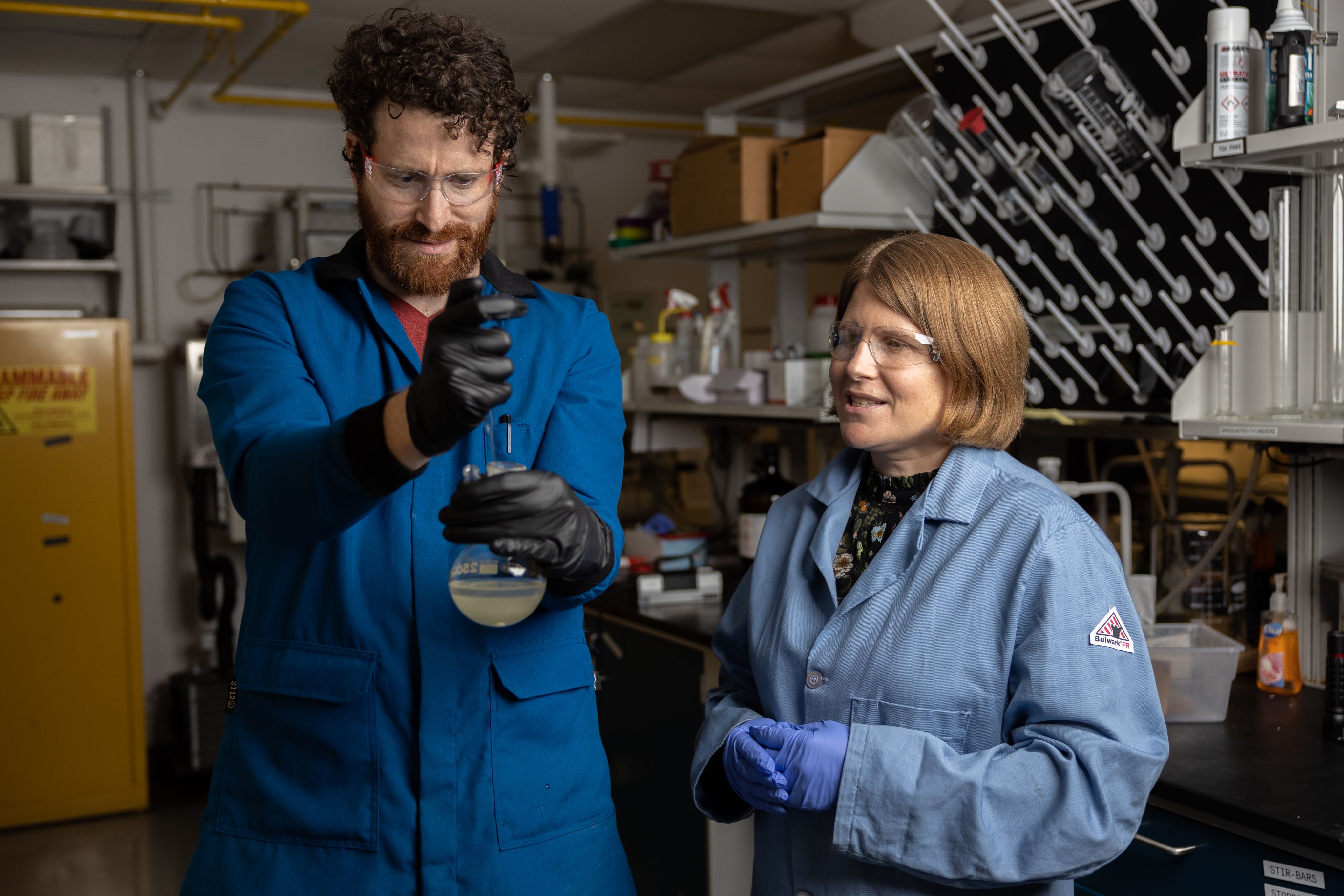 A male and female scientist working together in a lab, using a flask for experimentation.