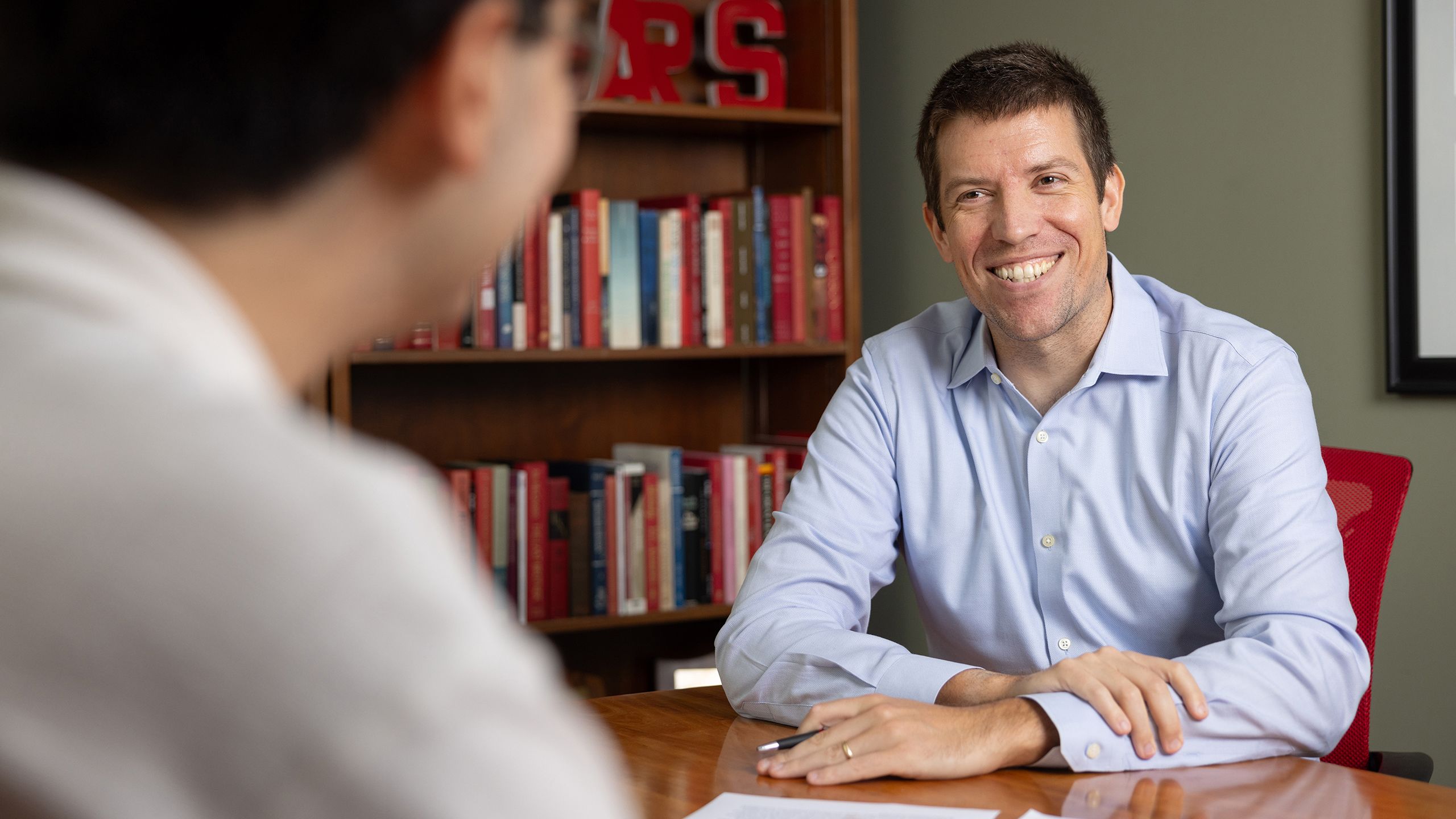 Ben Rayder smiles and talks to a student in his office.