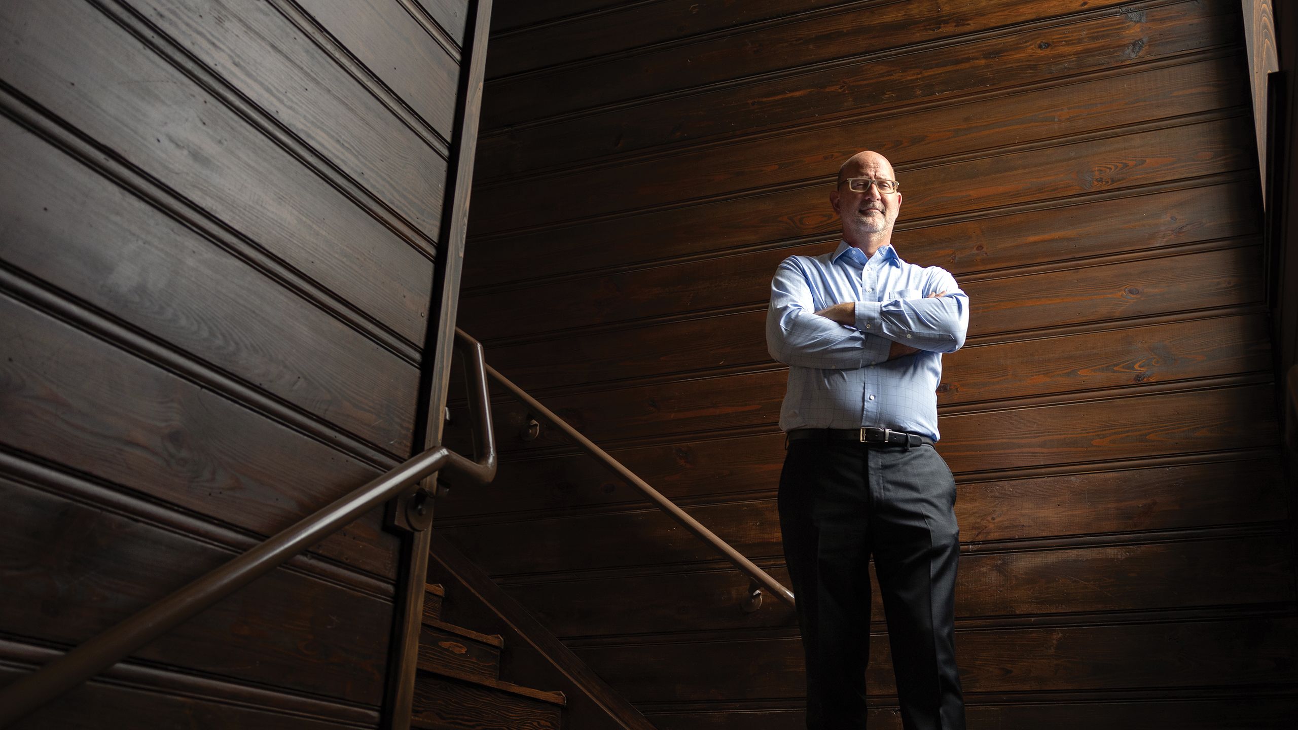 Portrait of David Bucek standing in a stairwell with his arms crossed.