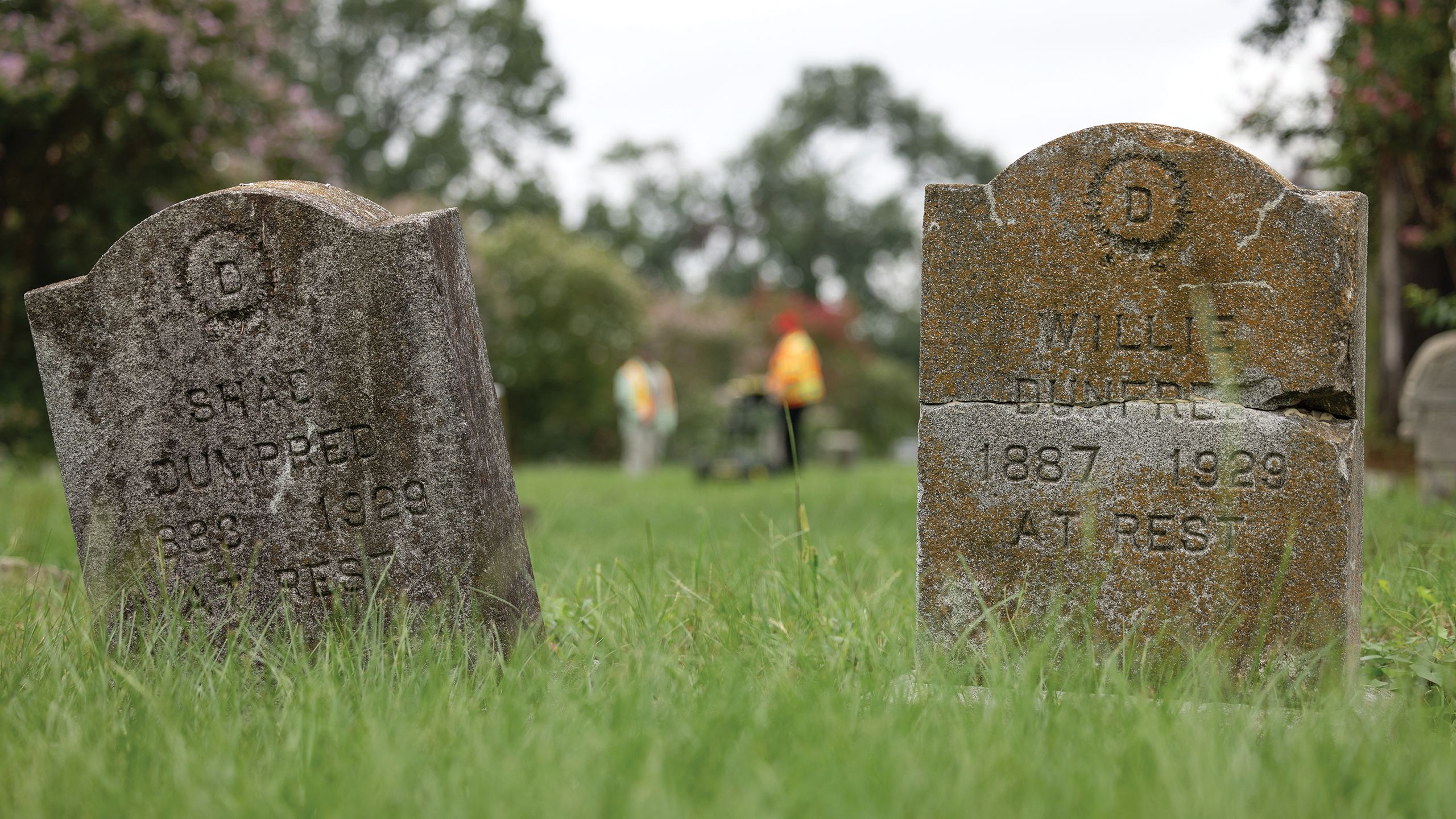 Two old gravestones at the Evergreen Cemetery with restoration technicians standing in the distance
