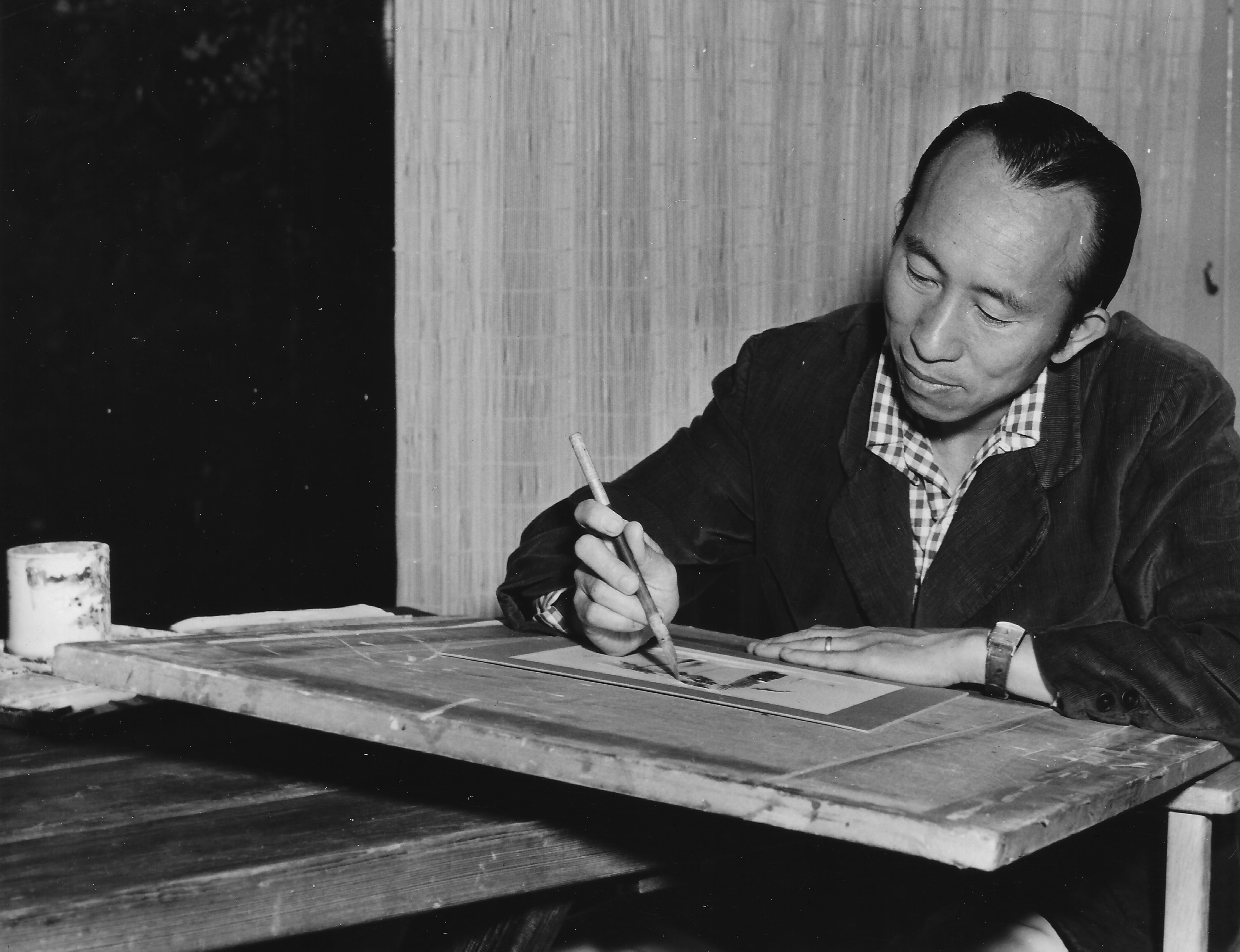A black-and-white photo of Tyrus Wong painting at an artist's table