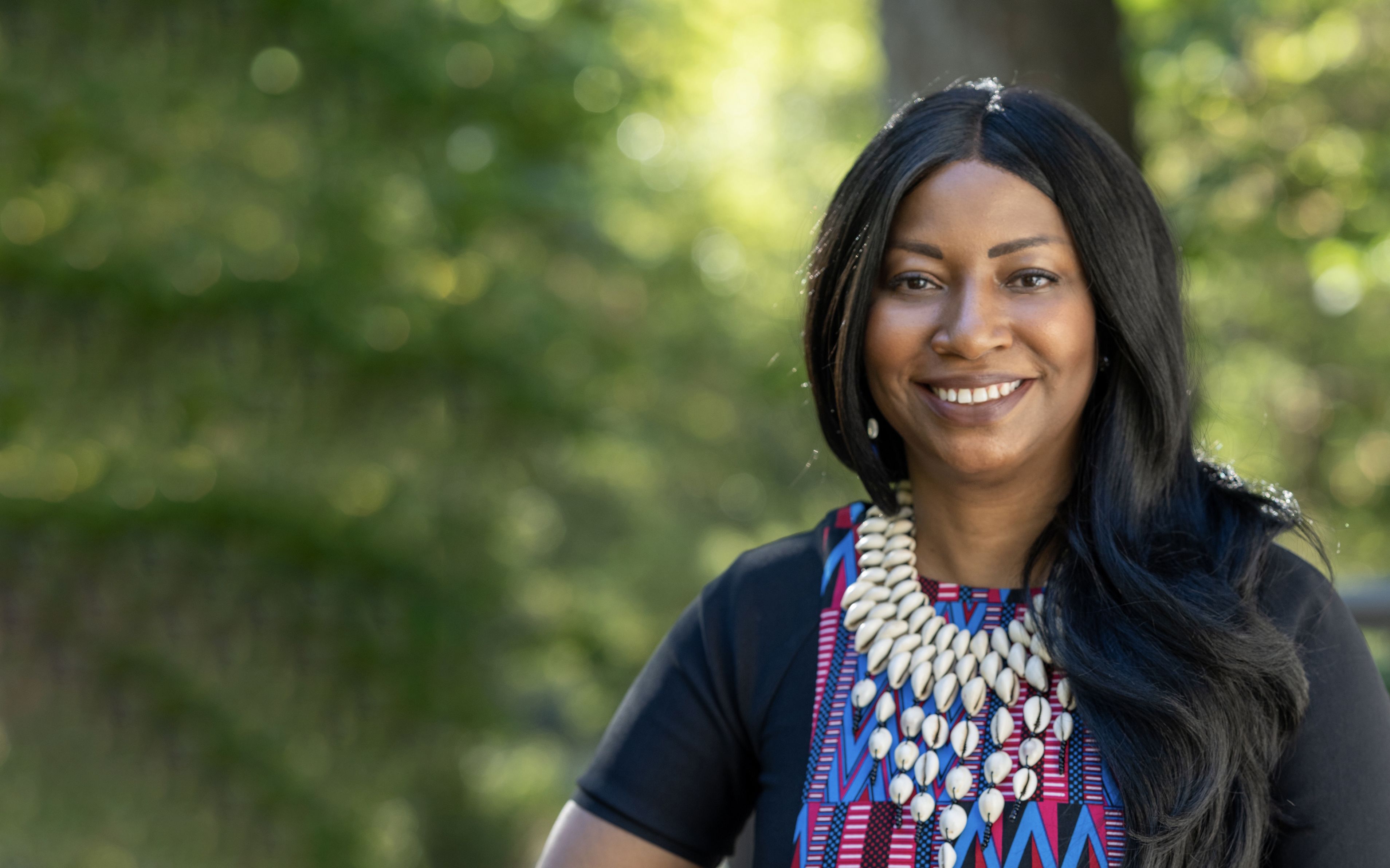 Tamar Evangelestia-Dougherty smiling at the camera in front of a tree.