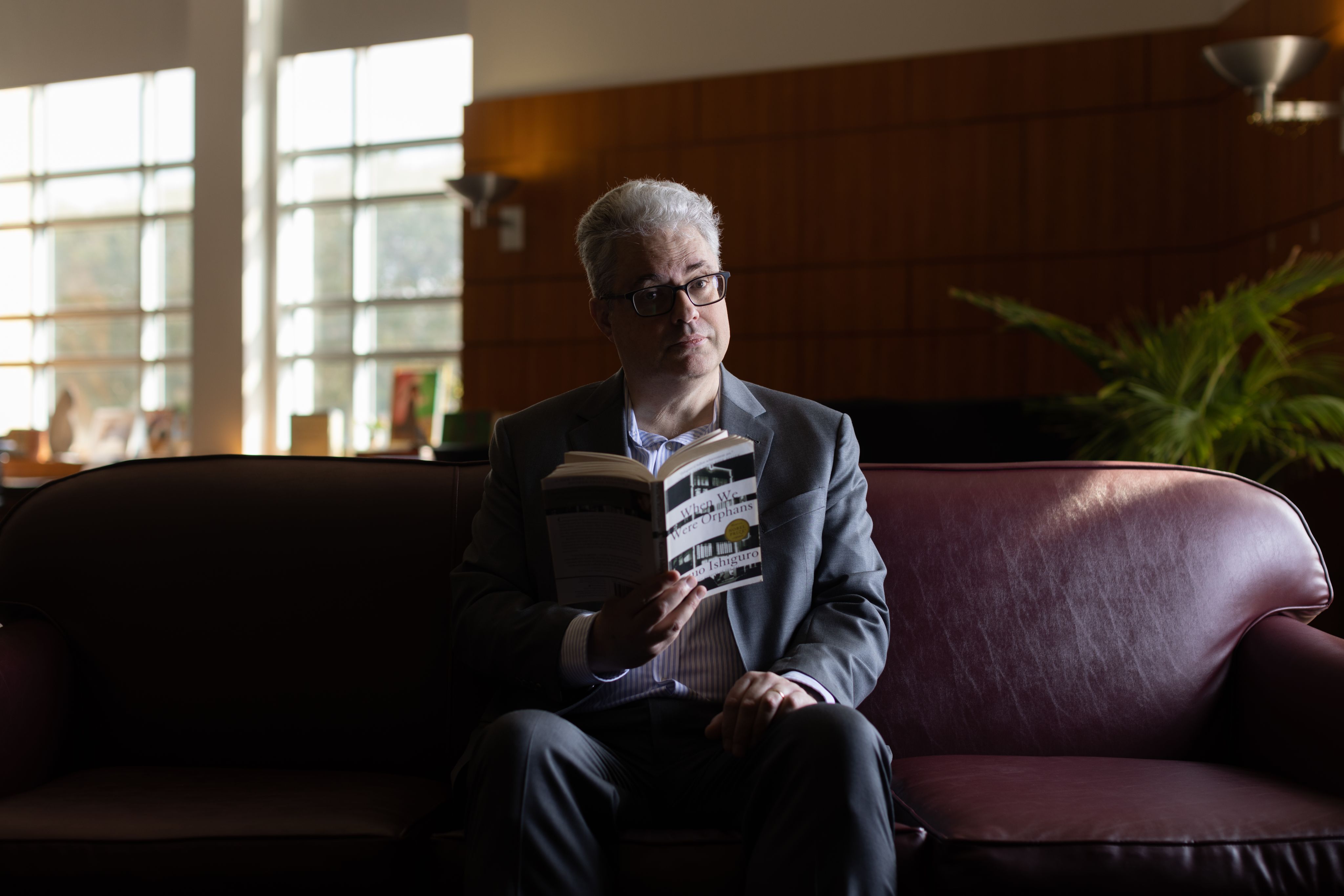 Robert Cremins on a couch, holding a book, looking at the camera.