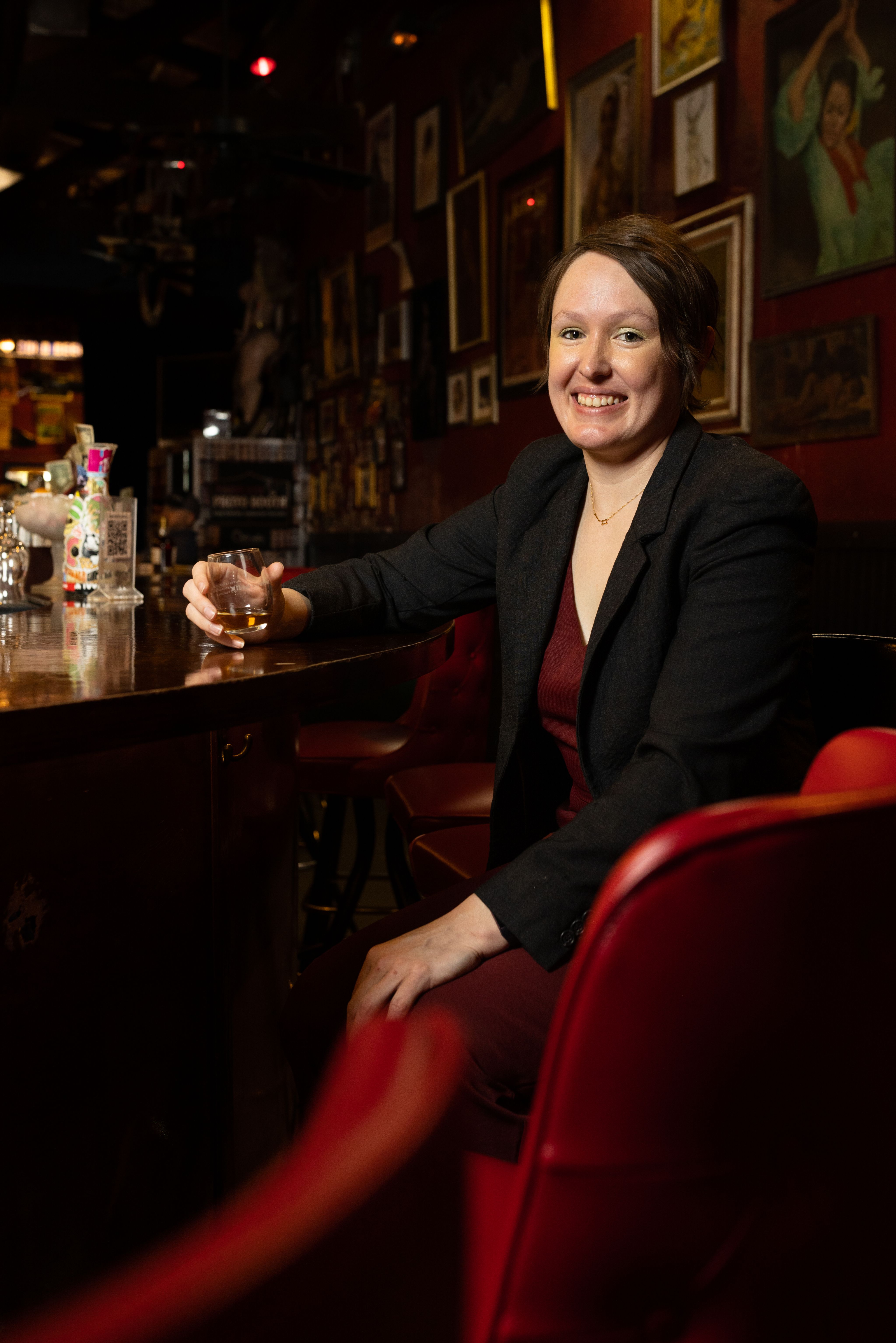 UH alum Blair Ault smiling while sitting at a bar, holding a glass of whisky.