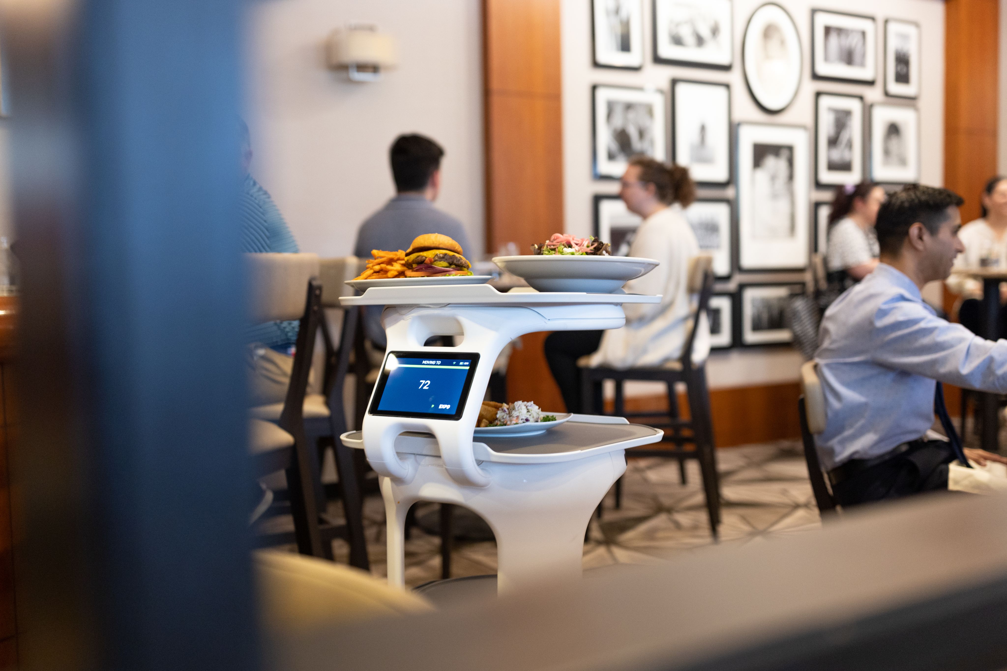 Servi the restaurant robot carrying a plate of food in the middle of a busy restaurant. 