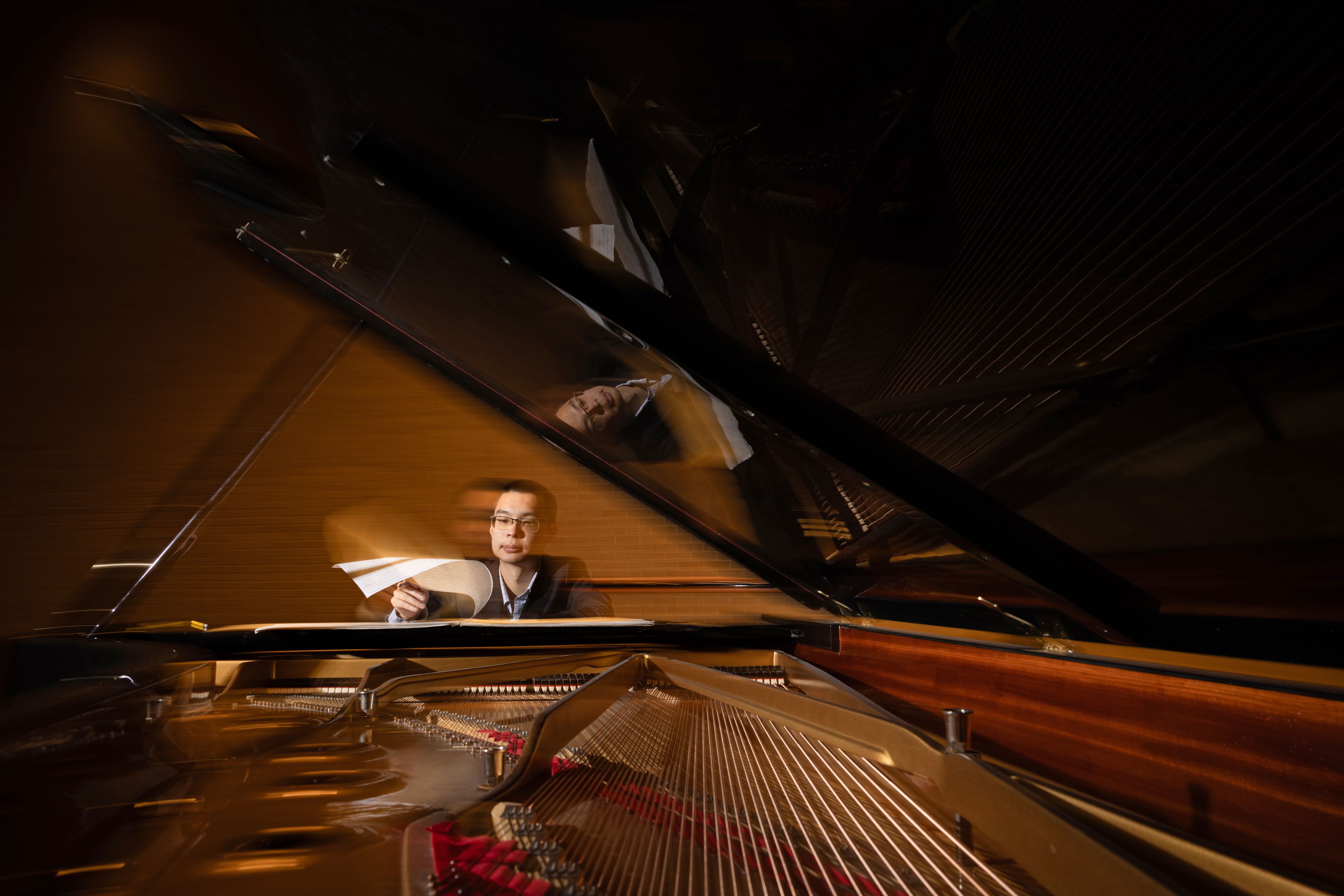 Sam Wu sits at a piano and holds sheet music.