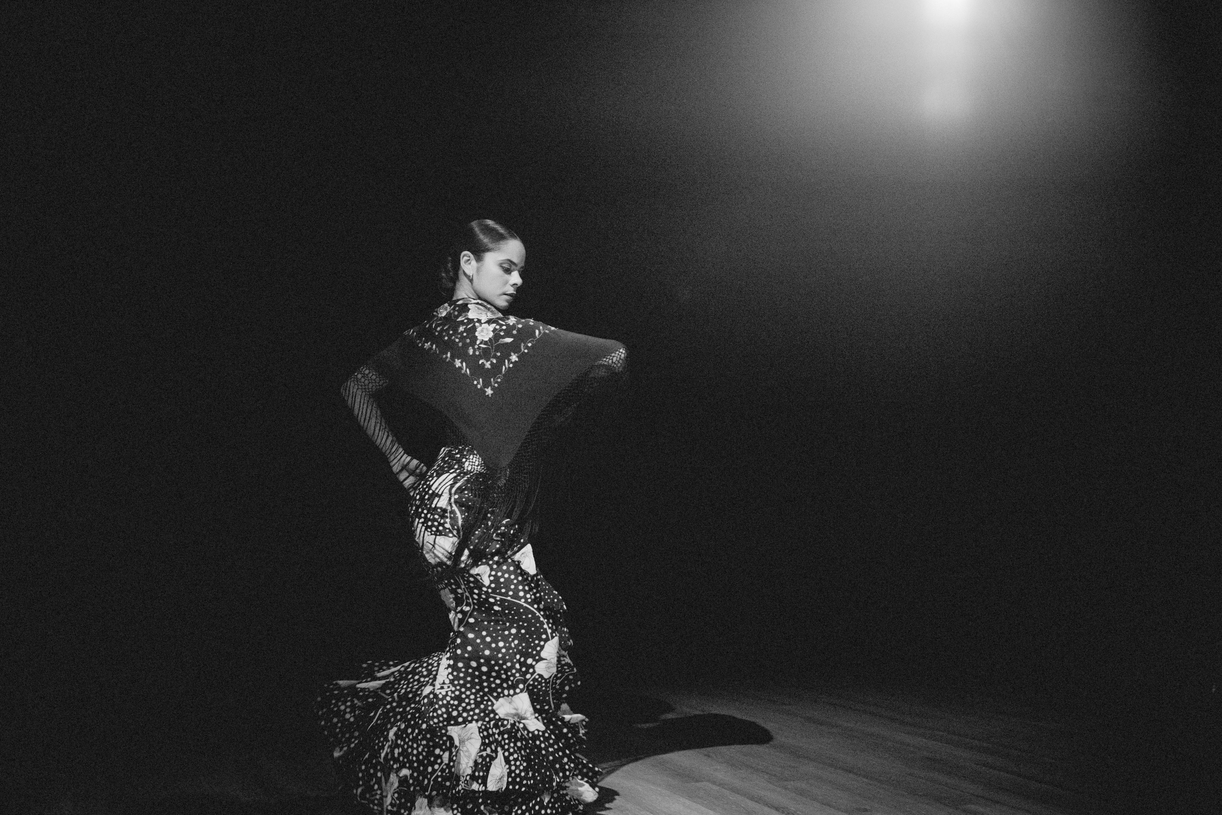 A woman in a long dress and shawl dances flamenco. 