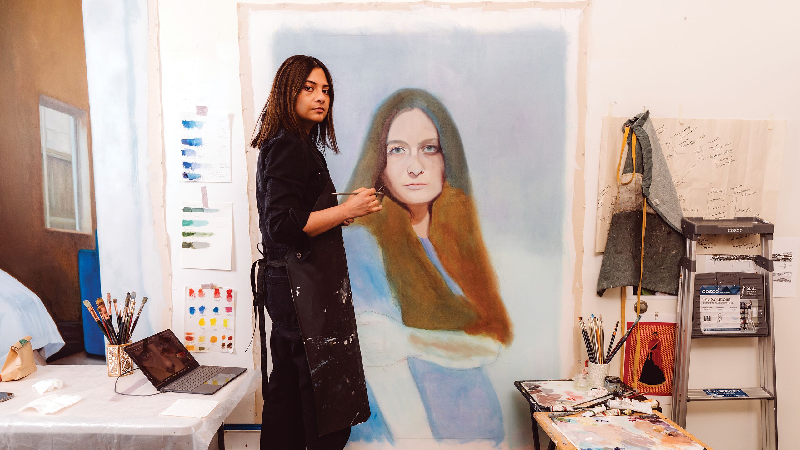 Sajeela Siddiq pauses from painting a portrait of a woman with long dark hair to pose for a photo
