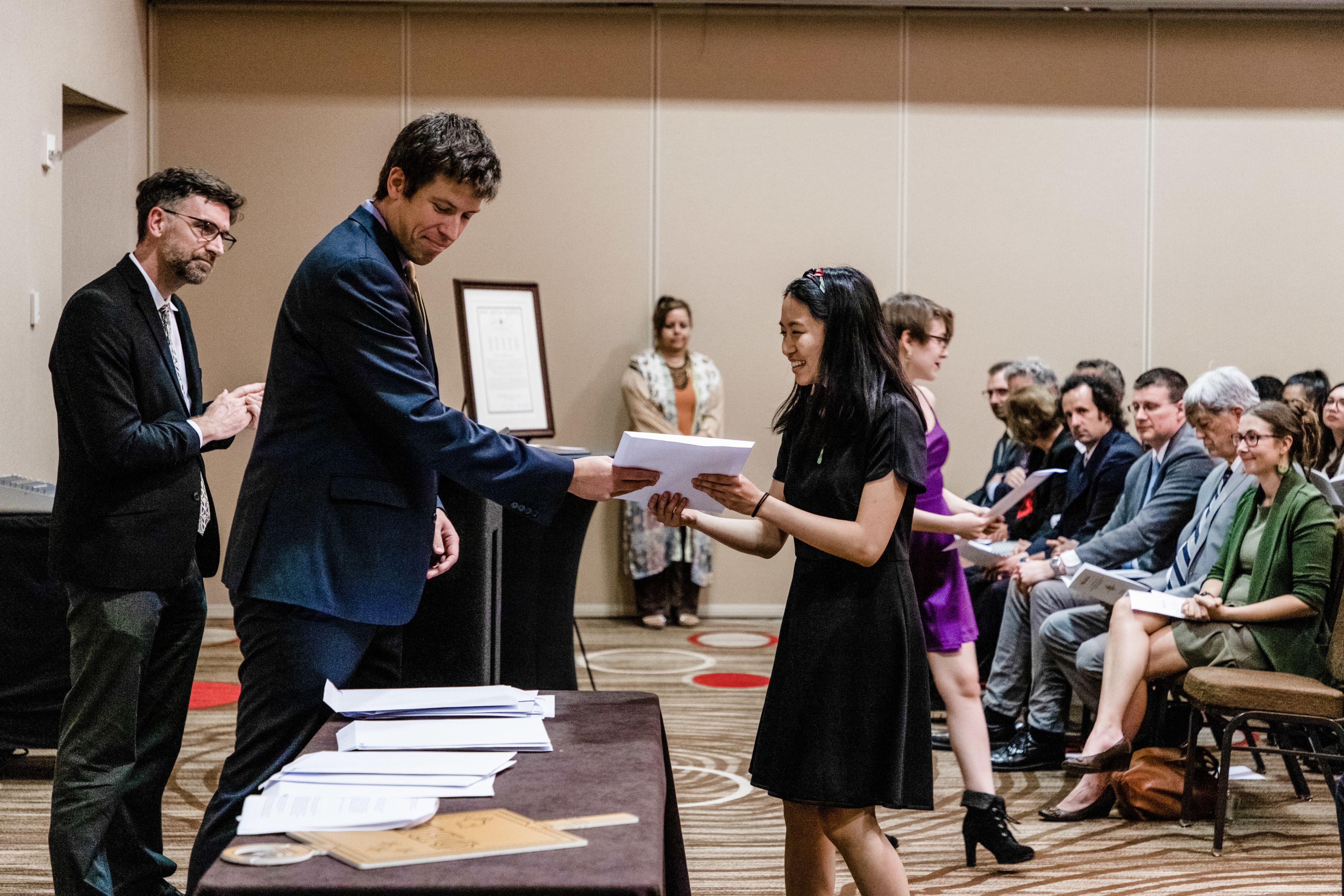 Man in suit handing girl in purplse dress a certificate