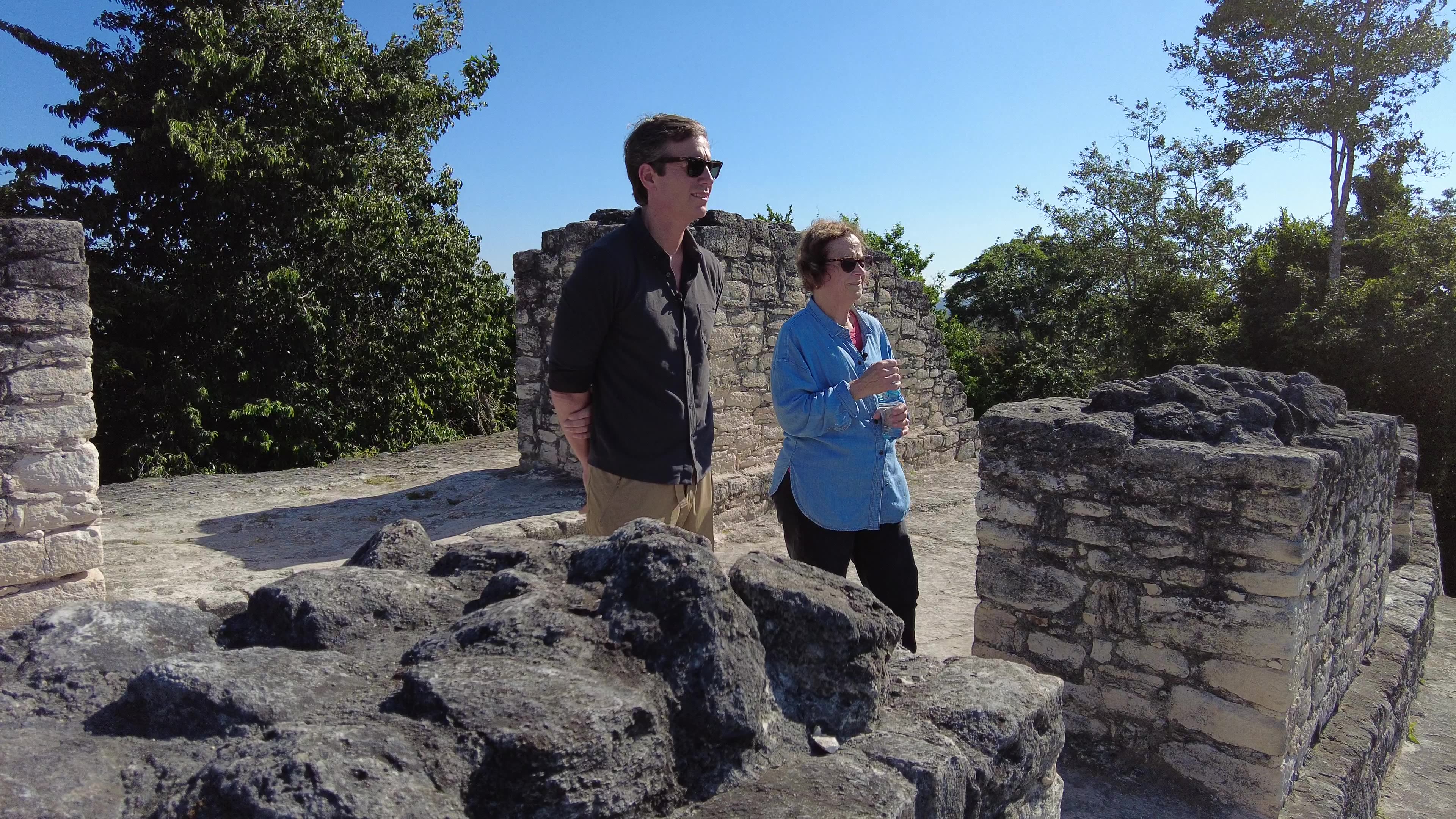 Man in black jacket standing with woman in blue jacket in archaeological site.