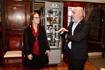 Woman with glasses, black dress and red scarf talking to a man with a black suit