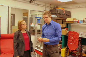 Woman with medium length hair and glasses, looking at taller man with short blonde hair, glasses and wearing blue shirt 