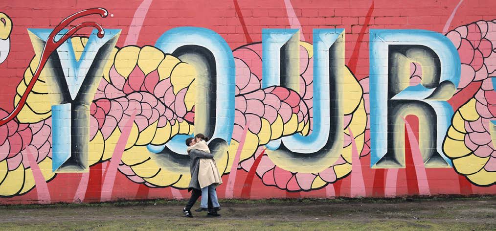 Two people hugging and kissing in front of the wall with artwork