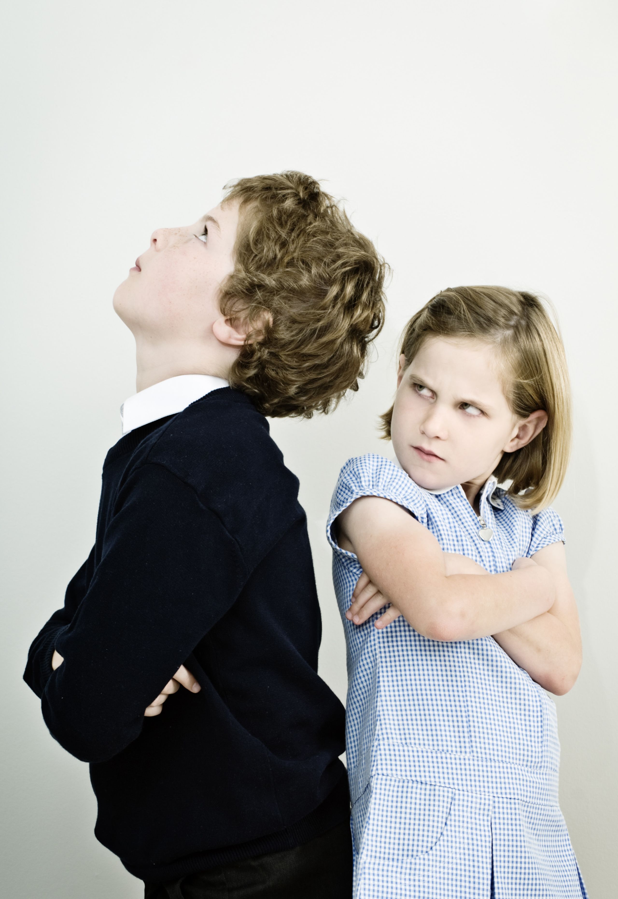 2 Kids standing back to back, one kid looking up and another kid looking next at the person with an expression of angry
